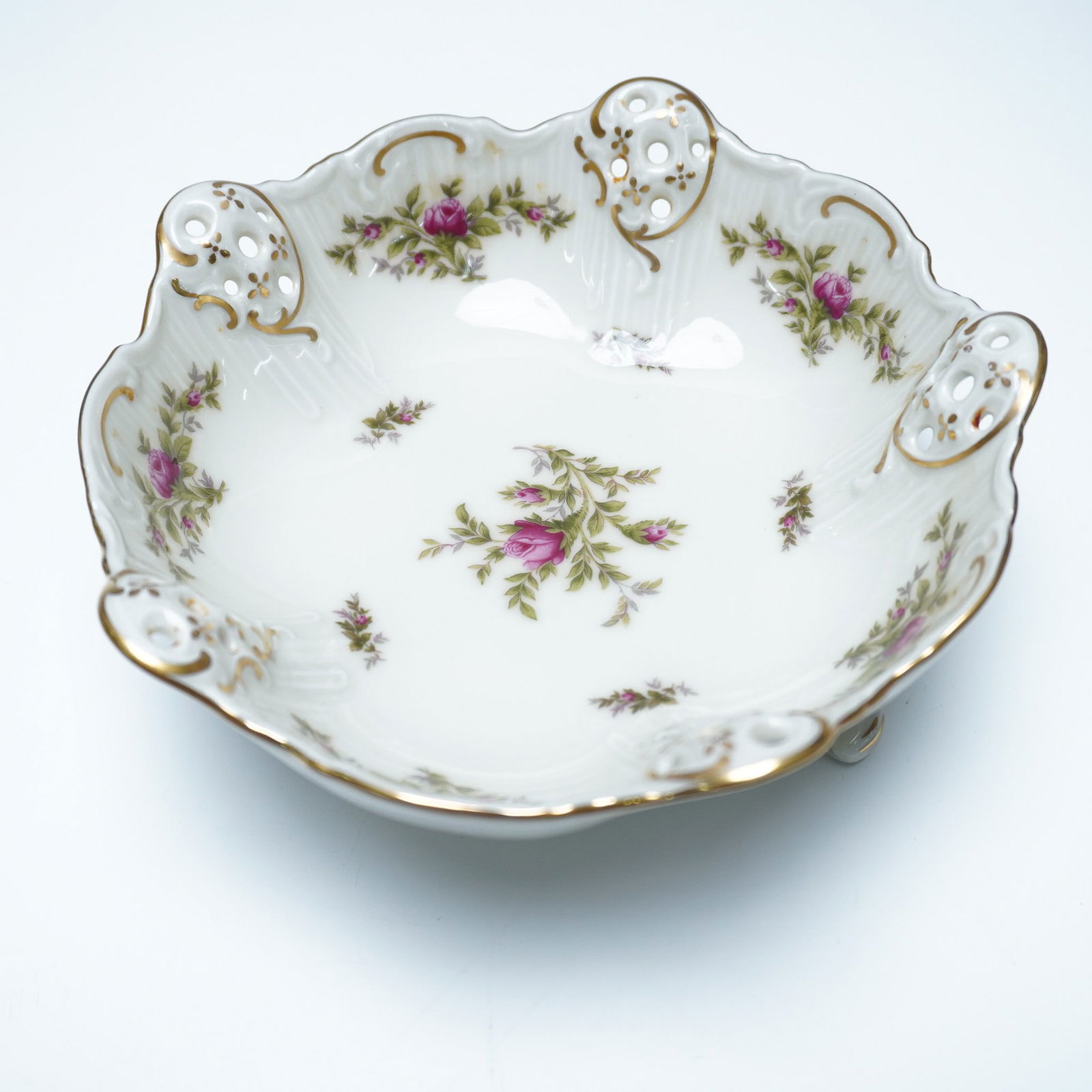 Rosenthal Pierced 3 Toed Bon Bon Bowl, Moss Rose: The porcelain bowl is elevated on three curved feet and features an openwork pierced rim with intricate detailing. The design includes applied rose motifs with floral sprays set against a white porcel