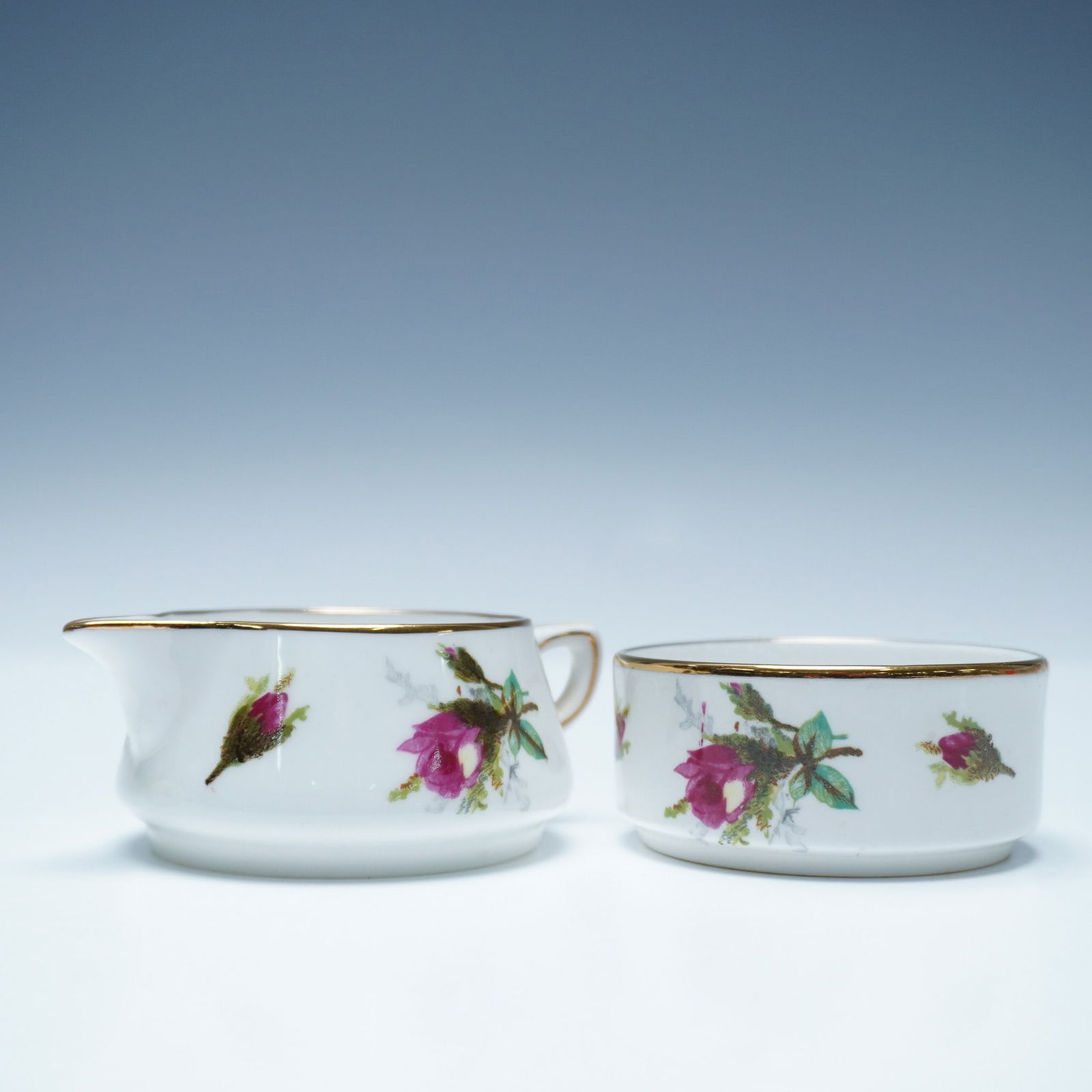 Pair Hammersley Sugar Bowl and Creamer, Grandmother's Rose: Bone china mini creamer and round sugar bowl featuring a pink rose motif on a white background with gold trim. The creamer has a curved spout and handle, while the sugar bowl has a smooth, rounded for