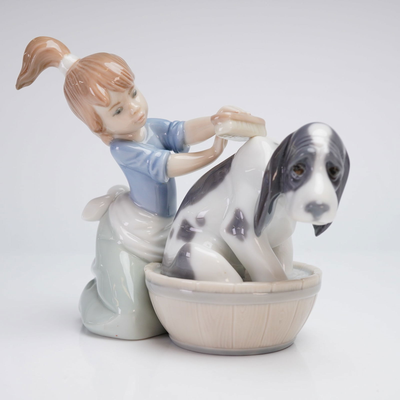 Lladro Porcelain Figurine, Bashful Bather 5455: This Lladro Bashful Bather glazed porcelain figurine, model number 5455, is a representative example of Lladro porcelain figurines depicting a young girl with a ponytail kneeling and washing a spotted