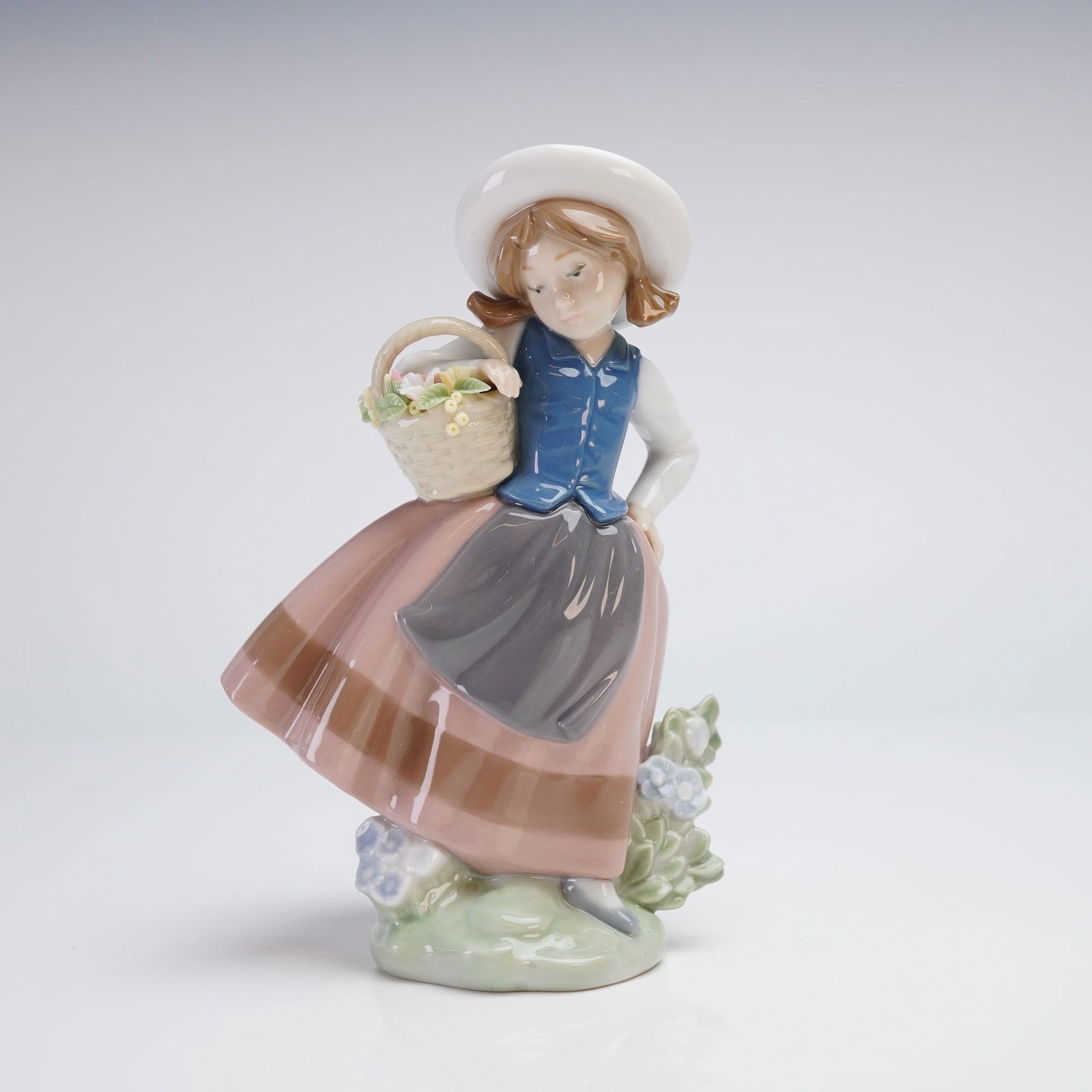 Lladro Porcelain Figurine, Sweet Scent 5221: A Lladro porcelain figurine titled Sweet Scent, model number 5221. This glazed porcelain figure depicts a young girl wearing a white sun hat, a blue vest, and a long pink skirt with a dark brown apron