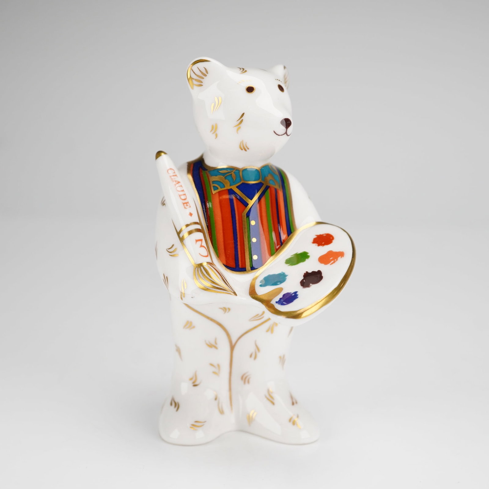 Royal Crown Derby Miniature Figurine, Teddy Bear Artist Claude: This anthropomorphic artist bear is depicted holding a paintbrush inscribed CLAUDE 3 and a palette with multi-colored paint. The figure is decorated with a colorful striped vest on the front and a blu