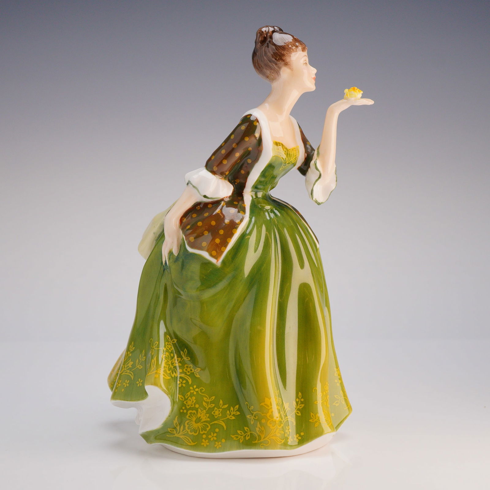 Royal Doulton Figurine Fleur HN2368: The figure depicts a woman in a sweeping period gown, predominantly colored in glossy dark green with yellow stylized floral accents, paired with a brown polka-dot jacket and cream accents. She is sho
