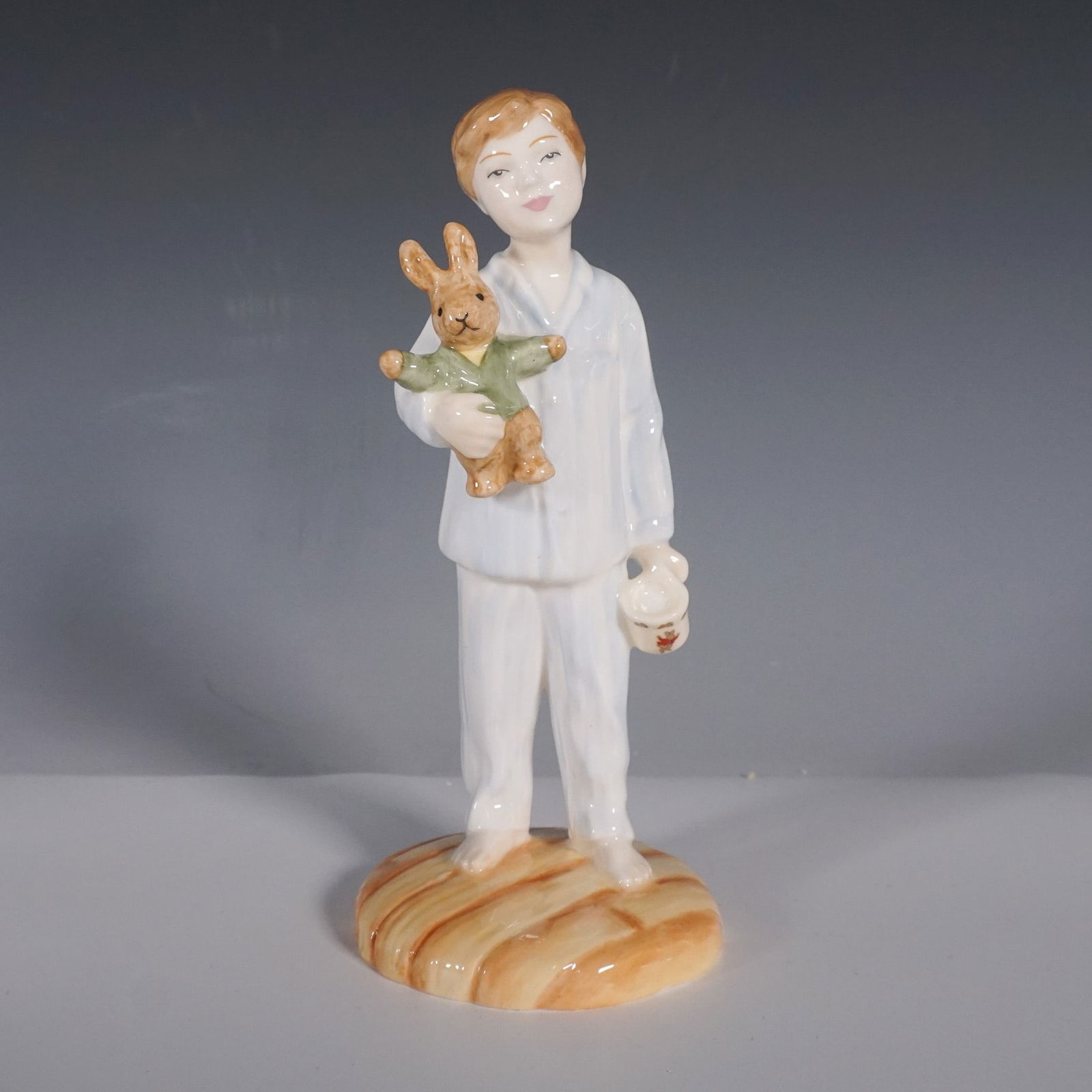 Royal Doulton Figurine, Lights Out HN4465: This charming Royal Doulton figurine titled Lights Out (HN4465) depicts a young boy dressed in pajamas holding a stuffed bunny, ready for bedtime. The porcelain piece was modeled by Annada M. Pedley a