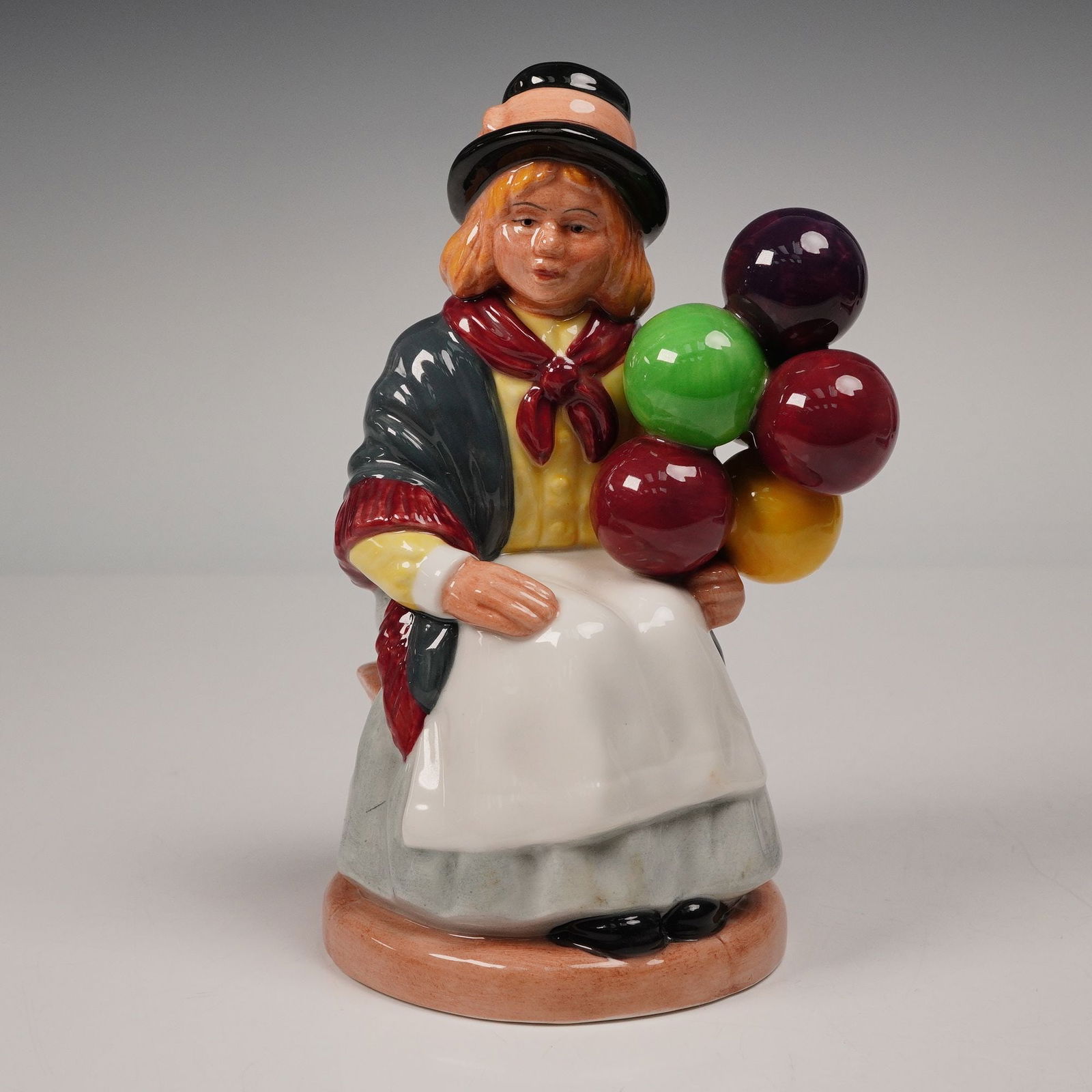 Royal Doulton Figurine, Balloon Girl HN2818: Charming Royal Doulton porcelain figurine titled Balloon Girl HN2818, designed by William K. Harper. The figure depicts a young girl in a bowler hat and shawl, seated with a colorful cluster of balloo