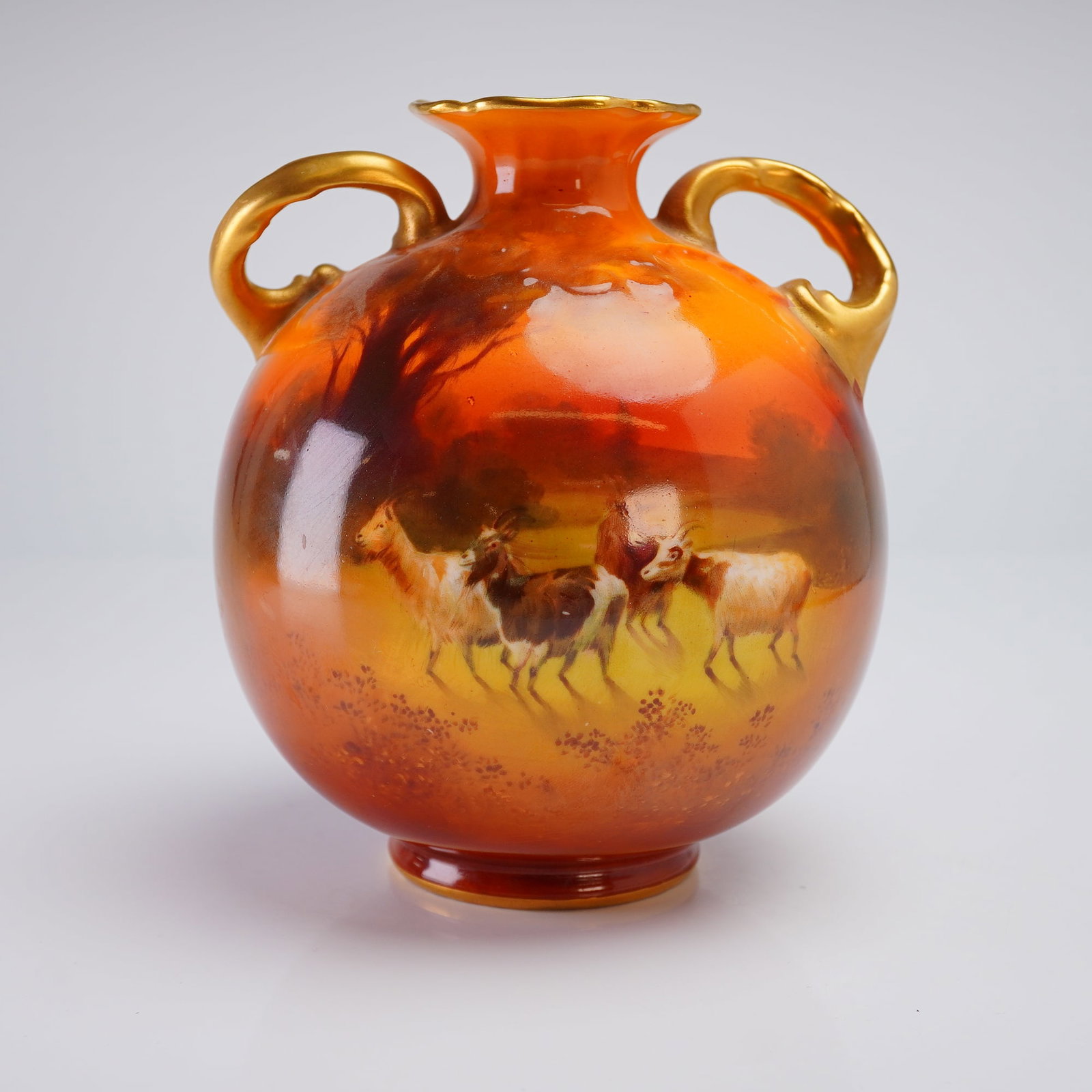 Royal Doulton Gilt Glaze Twin Handled Vase: The twin-handled vase is decorated with a high-temperature glaze transitioning dramatically from deep reddish-brown to bright orange. The central decoration is a polychrome transfer or enamel scene de