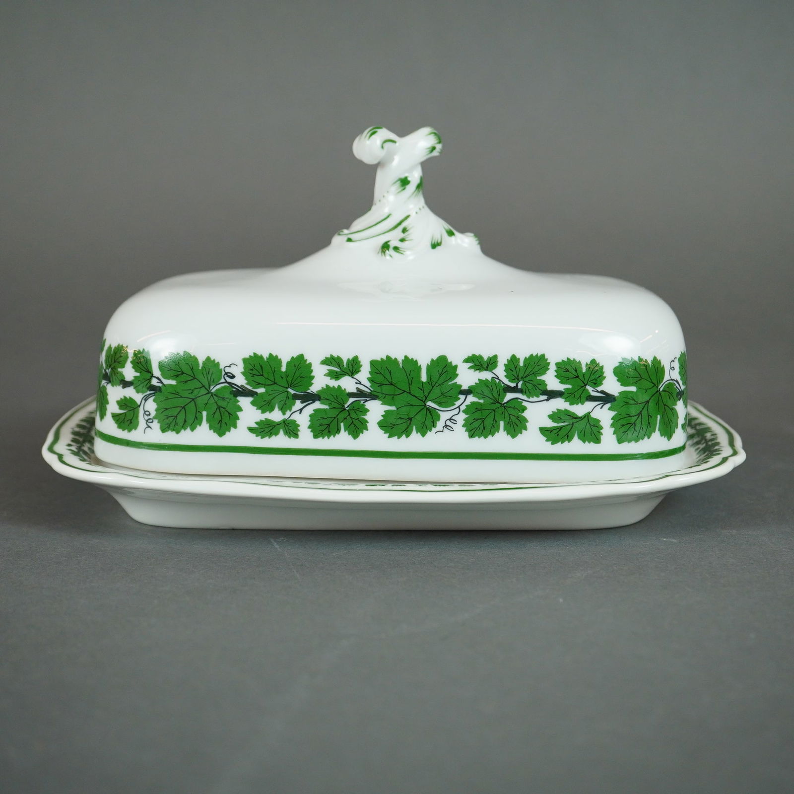 Meissen Full Green Vine Pattern Covered Butter Dish: A covered butter dish attributed to the Meissen porcelain manufactory, executed in the Full Green Vine pattern. The lot consists of two pieces: a rectangular base tray and a domed cover. The white por