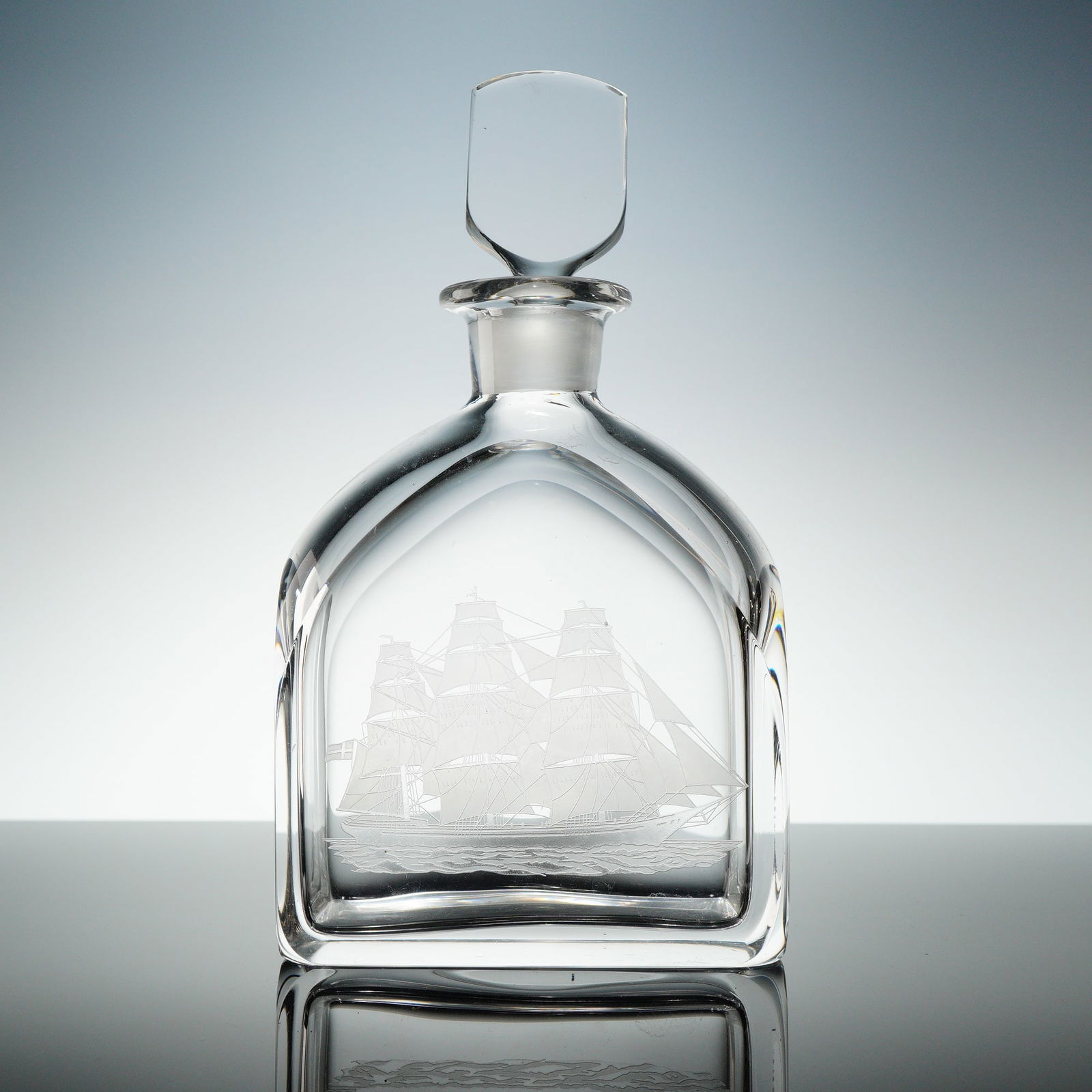 Orrefors Engraved Ship Motif Crystal Decanter with Stopper: A heavy, clear Orrefors crystal decanter with stopper, atributed to Edward Hald. The lot consists of two items: the decanter vessel and its matching faceted shield-shaped stopper. The decanter feature