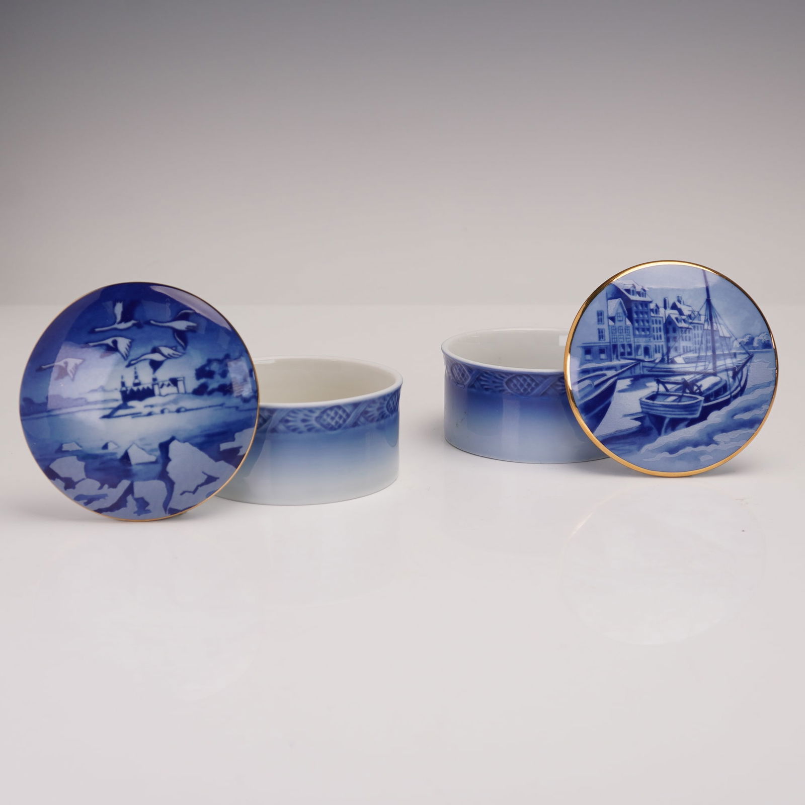 4pc Royal Copenhagen Porcelain Covered Boxes: A pair of Royal Copenhagen porcelain covered boxes, each decorated in traditional cobalt blue with gilded rims. One features a scene of Kronborg Castle with geese in flight, marked "Kronborg Castle" t