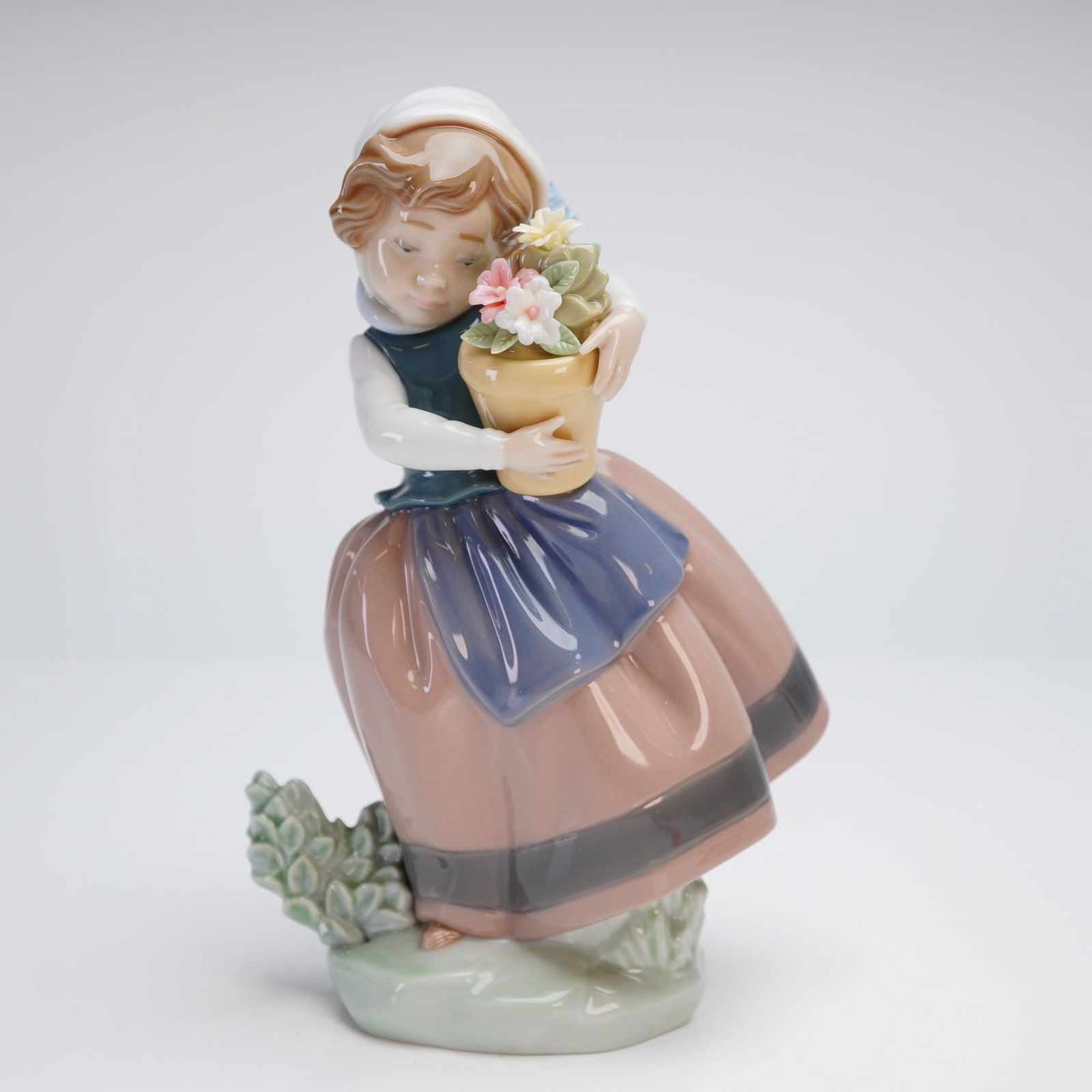 Lladro Porcelain Figurine, Spring is Here #5223: This Lladro porcelain figurine, titled Spring is Here, model number 5223, is a retired piece from the Lladro collection. The glazed porcelain figure depicts a young girl in traditional attire holding