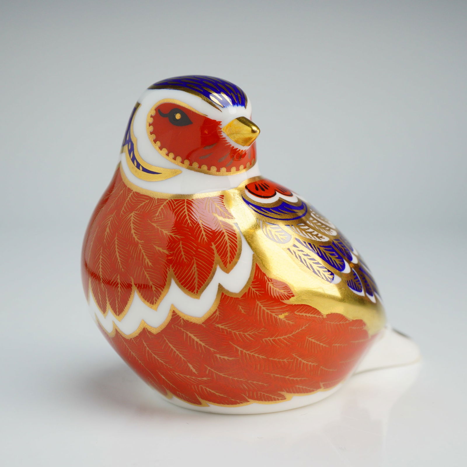 Royal Crown Derby Paperweight, Chaffinch with Box: The figurine is decorated in a palette of red, cobalt blue, and white, with fine-line gold gilding highlighting the plumage. The underside features a gold-toned stopper, and a red factory backstamp wi