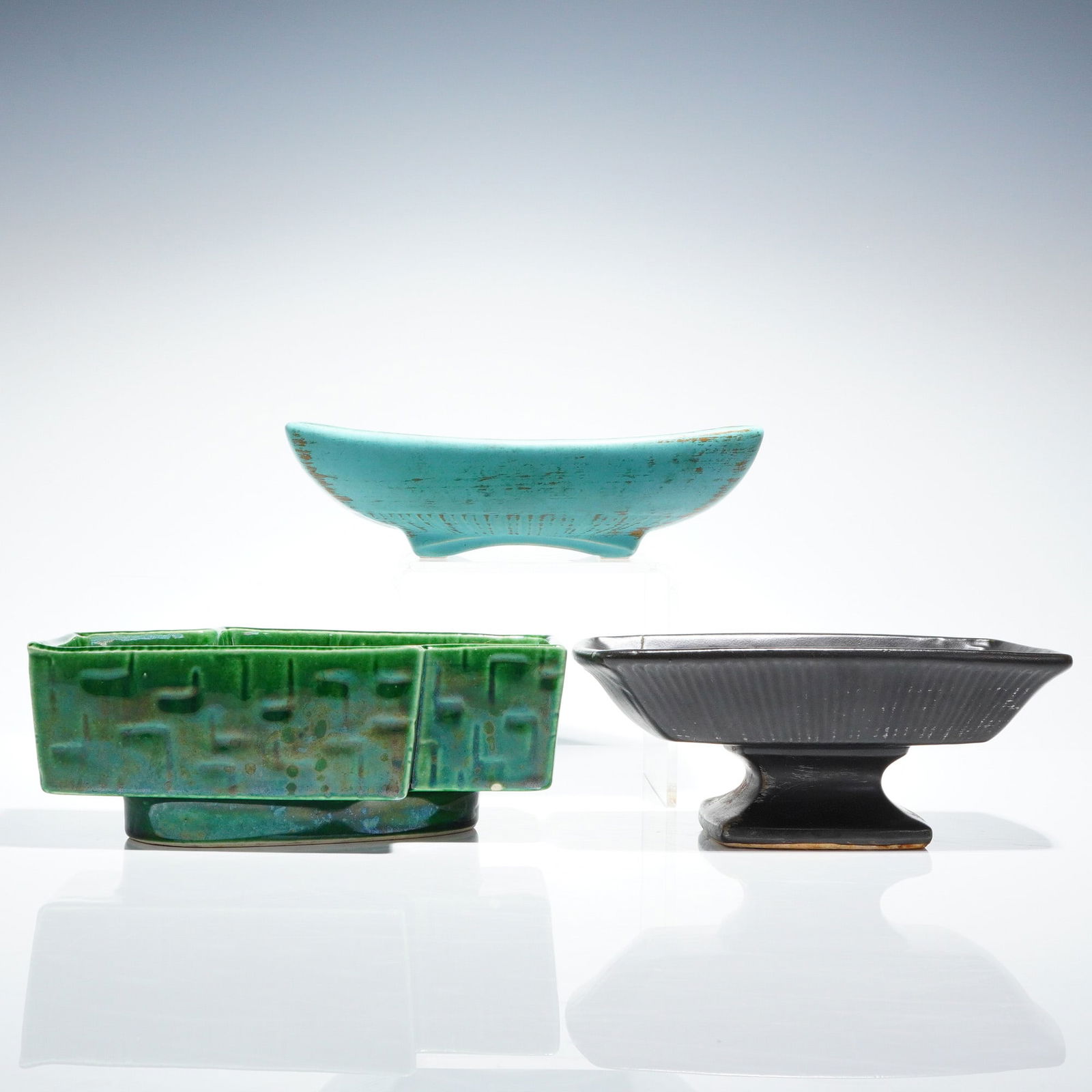 A Trio of Mid-Century Modern McCoy Pottery Planters and Dishes: A collection of three (3pc) vintage McCoy Pottery planters and dishes executed in glazed earthenware, reflecting a Mid-Century Modern aesthetic. The collection includes a boat-shaped vessel finished i