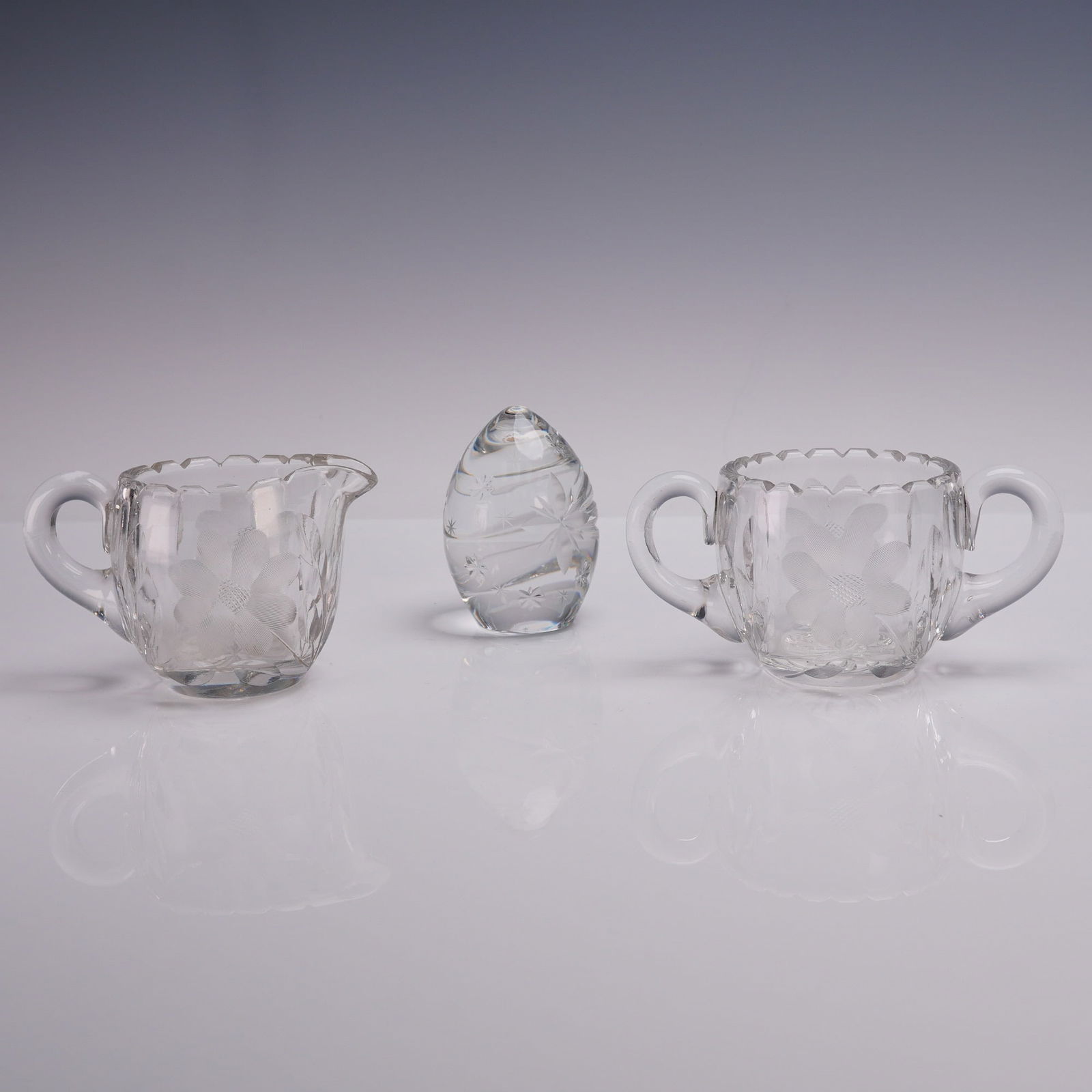 3pc Cut Glass Creamer and Sugar Set with Sullivans Egg Paperweight: Clear glass creamer and sugar bowl set, each featuring a cut glass floral pattern with scalloped rims and white applied handles. The creamer has a single handle and spout, while the sugar bowl include