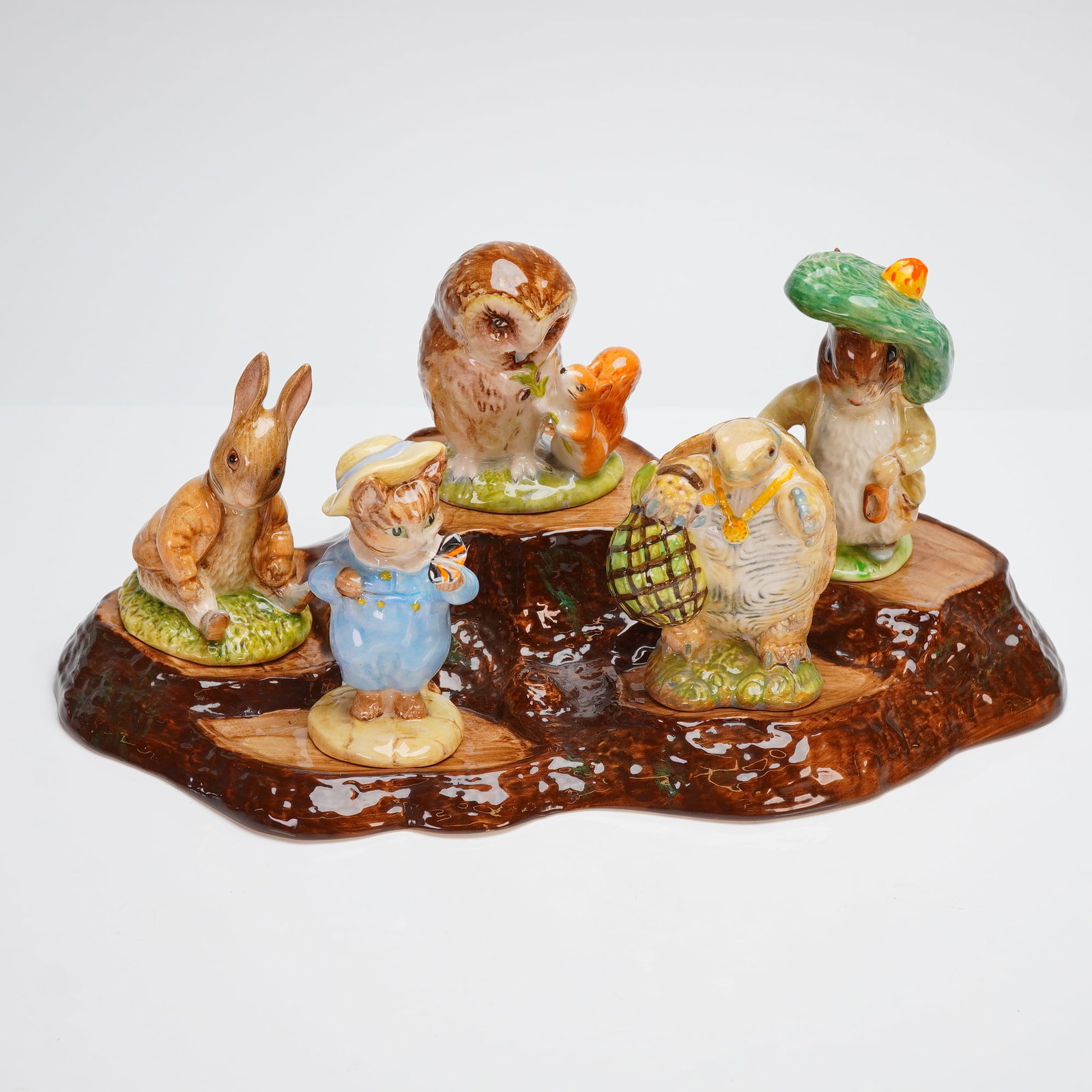 6pc Royal Albert and Beswick Beatrix Potter Figurines with Tree Stump Base: A collection of five Beatrix Potter figurines, featuring Benjamin Bunny Sitting on a Bank and Mr. Alderman Ptolemy, both from Royal Albert and signed by Michael Doulton. The set also includes three Be