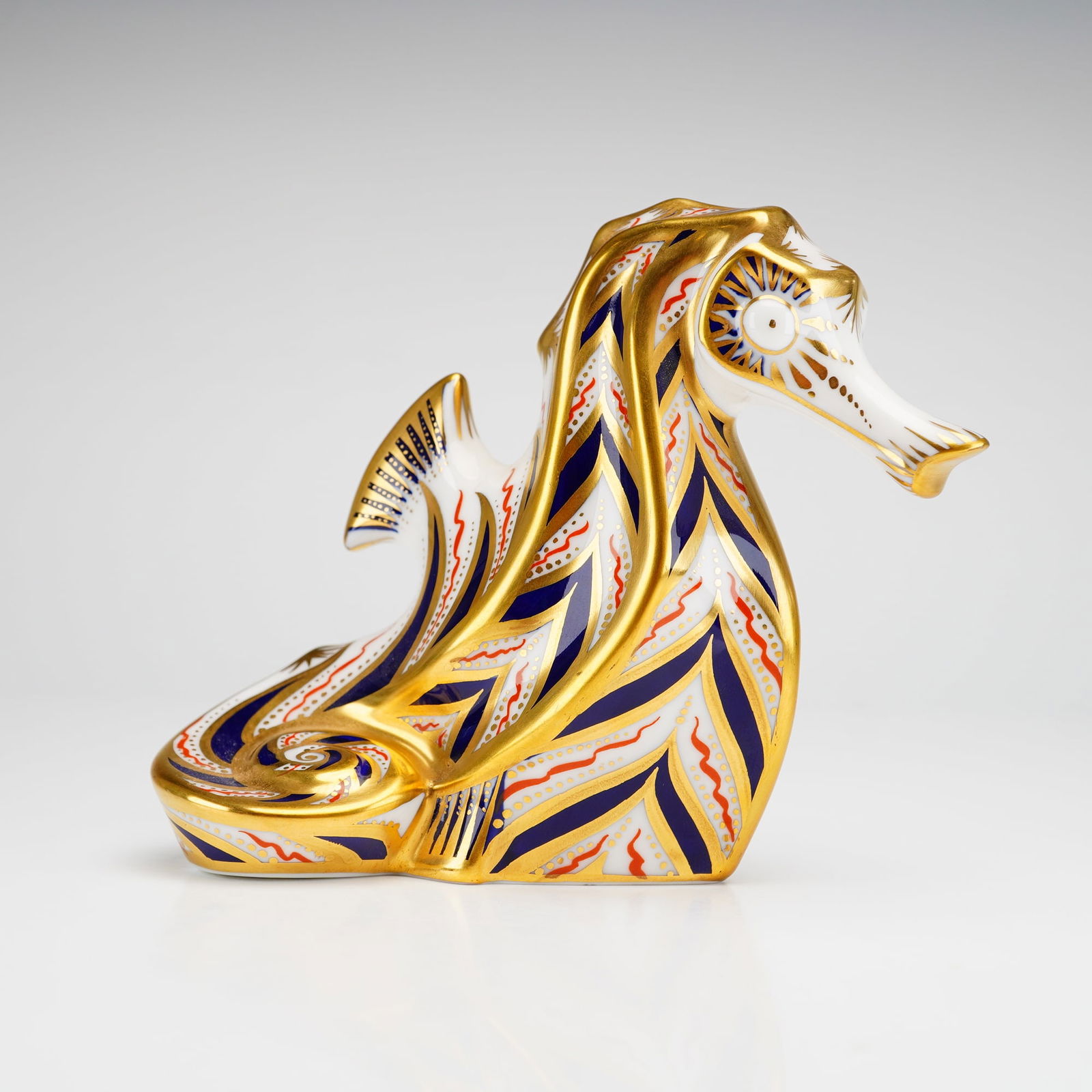 Royal Crown Derby Old Imari Solid Gold Band Paperweight, Sea Horse: The figurine features a palette of cobalt blue and iron red with heavy burnished gold accents. The surface decoration includes geometric bands, wave motifs, and fine dotting. The underside is marked w