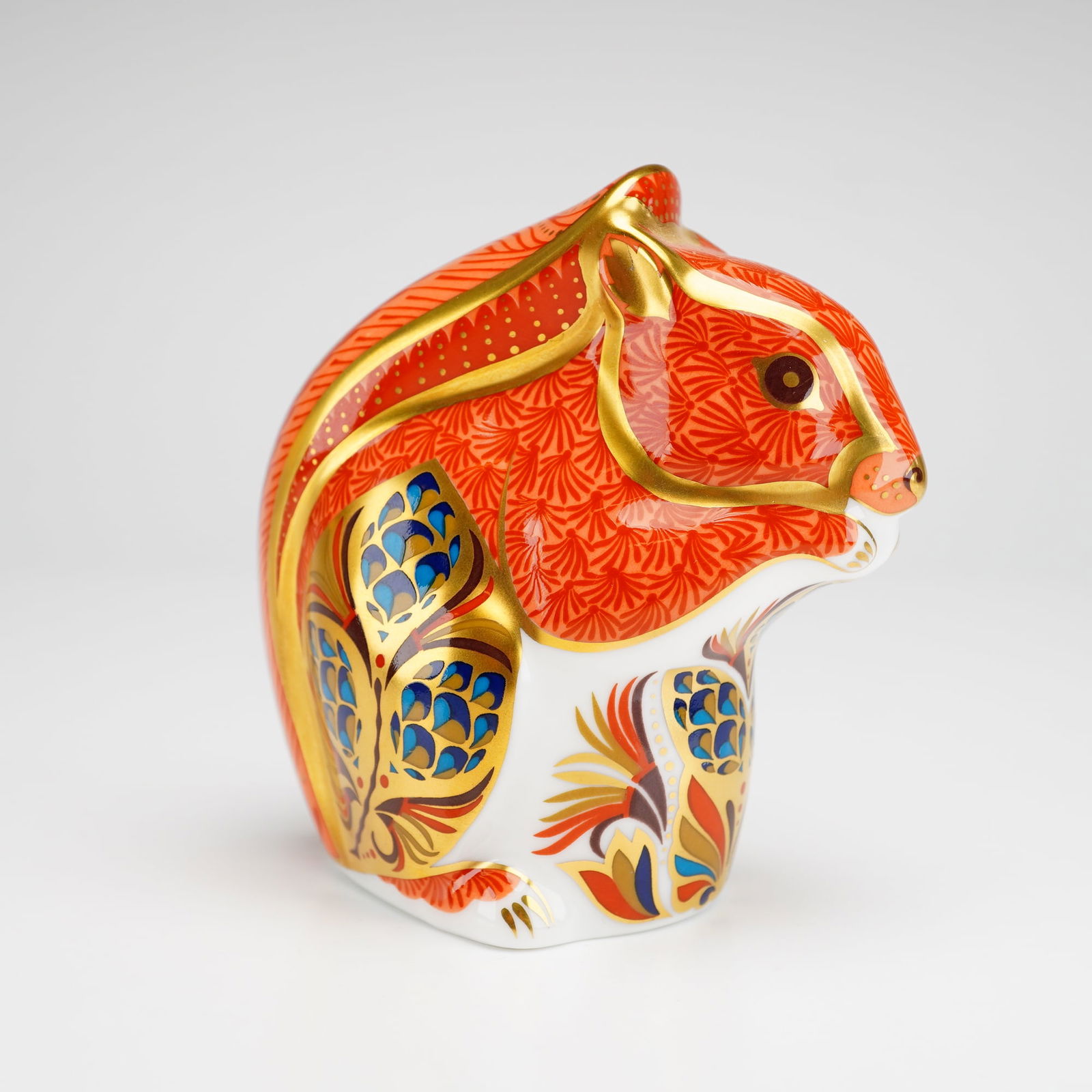 Royal Crown Derby Bone China Paperweight, Red Squirrel: The piece is decorated in a traditional Imari style, featuring an orange-red ground with stylized floral and foliate motifs in cobalt blue and gold. The figurine is finished with extensive gold gildin