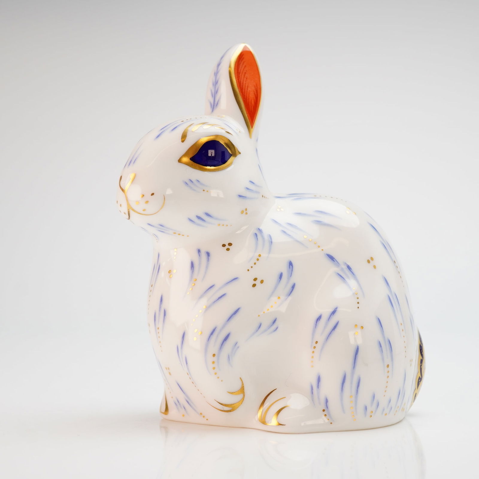 Royal Crown Derby Snowy Rabbit Paperweight with Box: A Royal Crown Derby fine bone china paperweight titled Snowy Rabbit. This figurine features a stylized design with cobalt blue and gold accents on a white ground. Modeled by John Ablitt and designed b