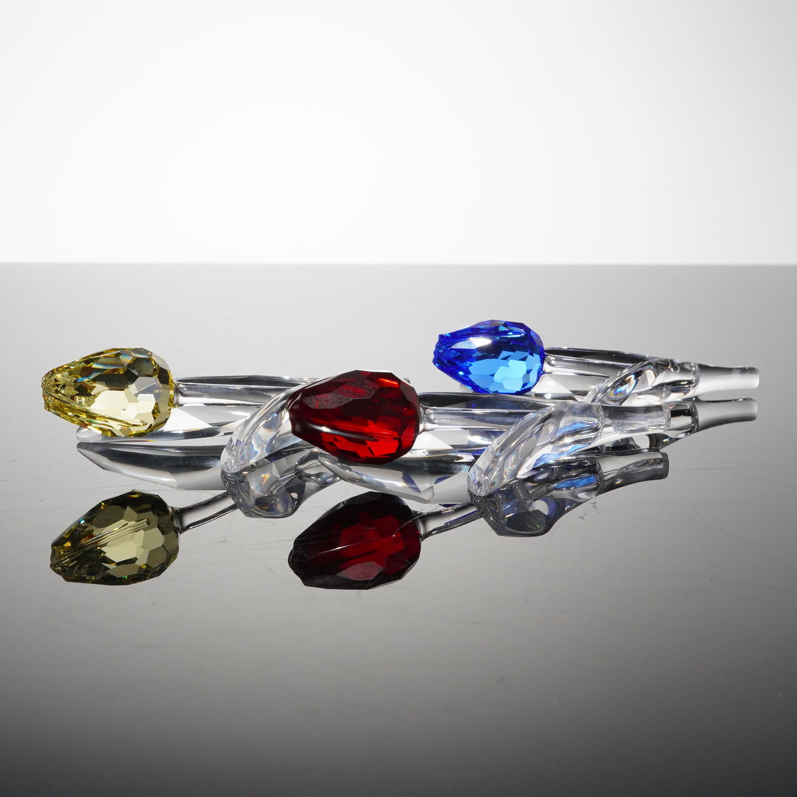 3pc Swarovski Crystal SCS Renewal Tulip Figurines: A collection of three individual crystal tulip sculpture, each constructed from faceted clear crystal forming the stem and leaves, supporting a large, faceted, teardrop-shaped flower head. The flower