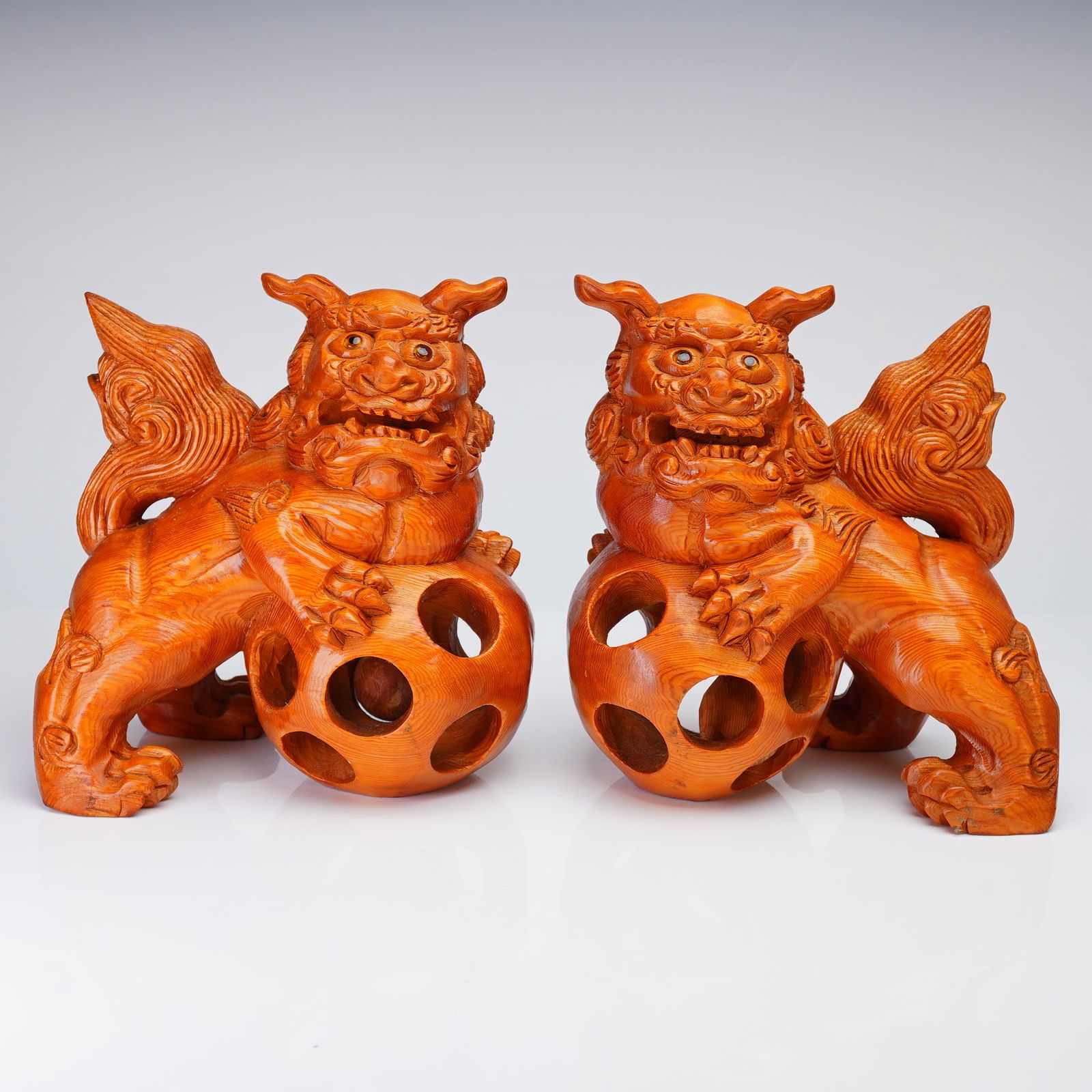 Pair of Chinese Carved Wooden Foo Dogs Resting on Pierced Balls: A pair of Chinese carved wooden Foo Dogs (guardian lion figures) resting on pierced balls. The figures are in carved wood and are depicted with fierce, open-mouthed expressions, dramatically rendered