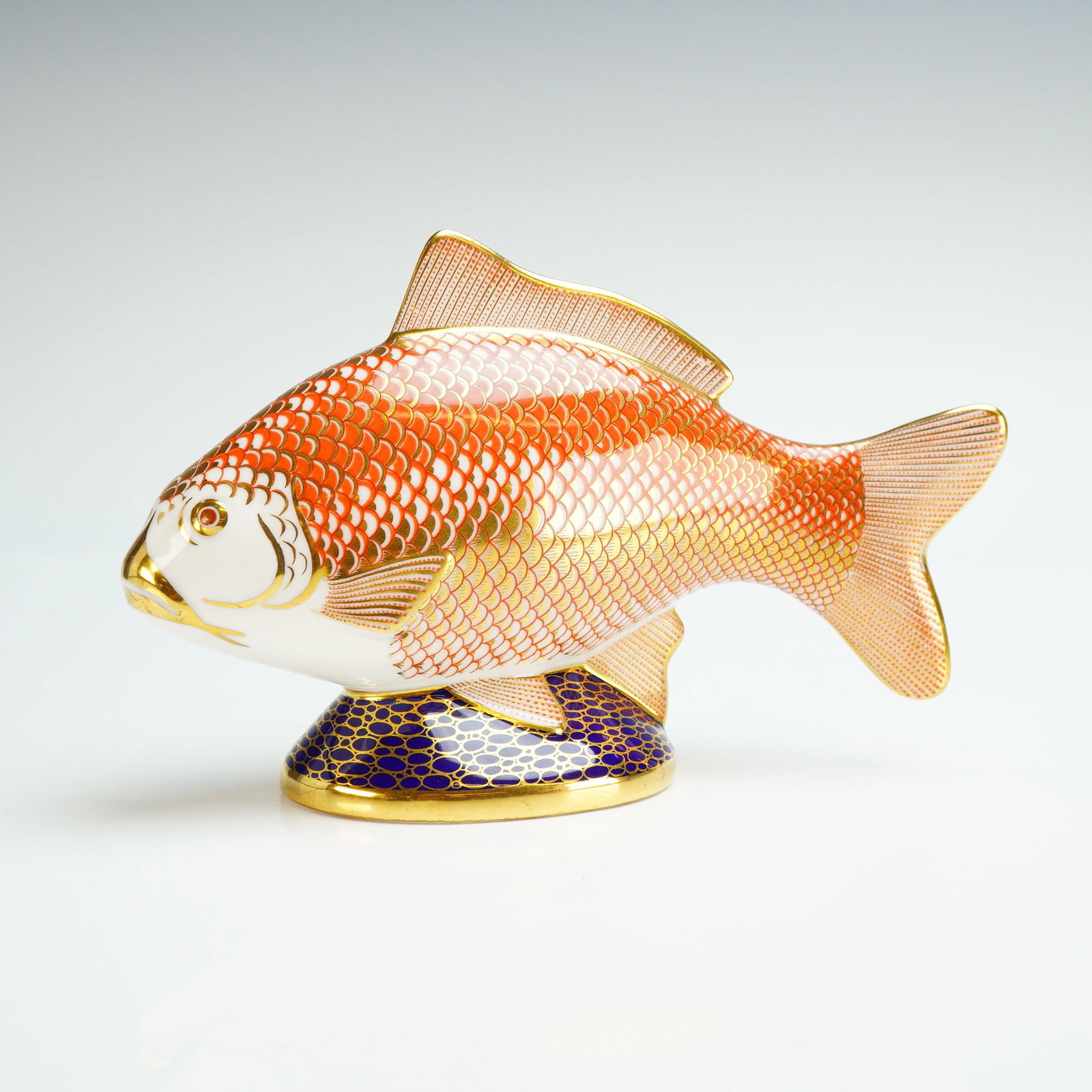Royal Crown Derby Paperweight, Golden Carp: The figure features an intricate Imari-style pattern with orange and gold scales over a white ground, resting on an integral oval base decorated with a cobalt blue and gold honeycomb motif. Gilt highl