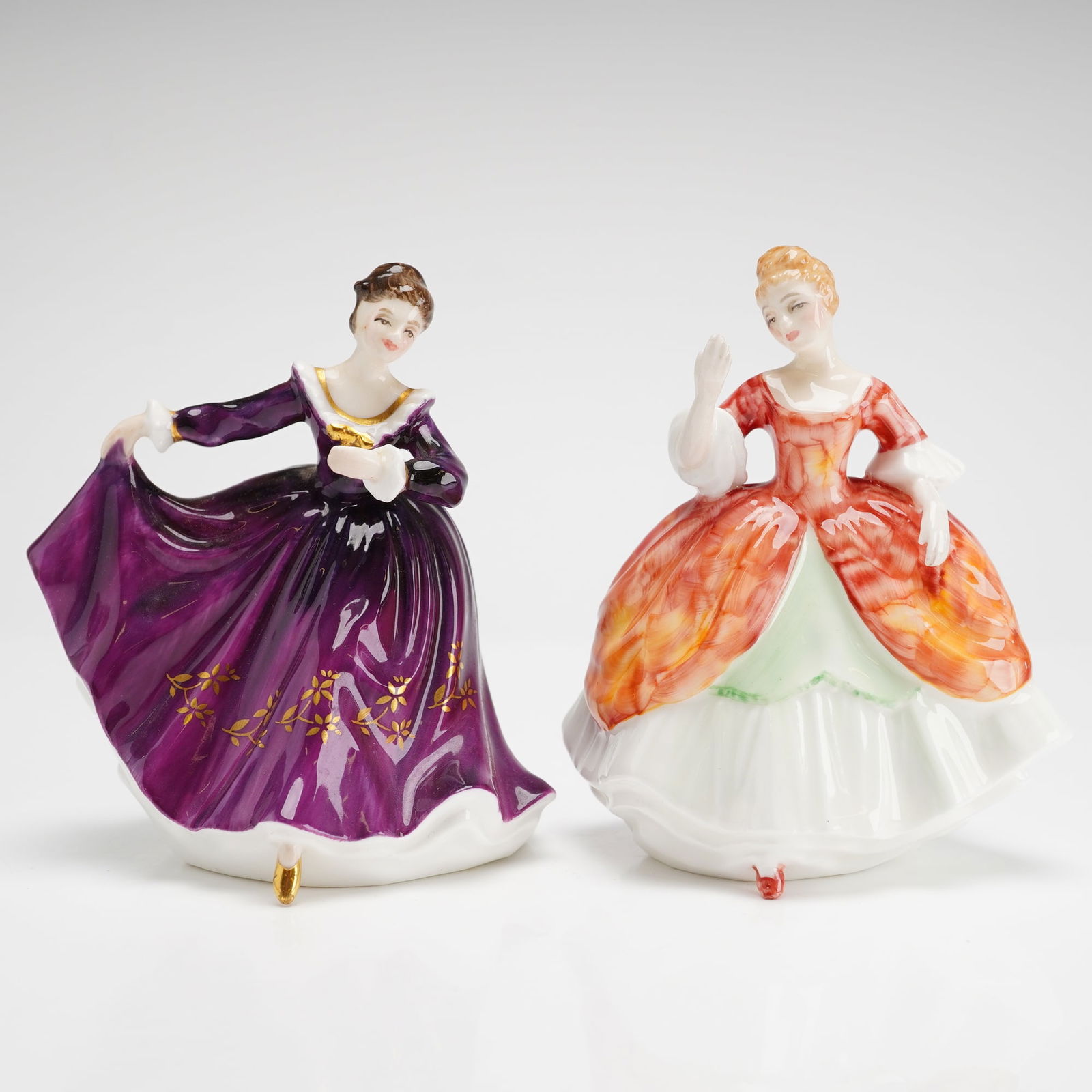 2pc Royal Doulton Mini Figurines Kirsty HN3246 and Christine HN3269: Each figurine is modeled in an 18th-century style gown. Kirsty is decorated in a deep plum glaze with gilded floral spray accents, and Christine is presented in a mottled orange and white ensemble. Th
