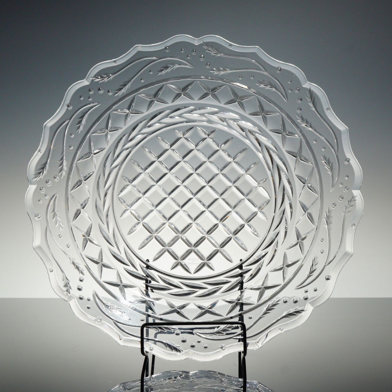 Marquis by Waterford Holly Pattern Crystal Platter: A round crystal platter from the Marquis by Waterford line, featuring a clear glass body with a scalloped rim. It is decorated with stylized flowing leaves and small raised beads, transitioning