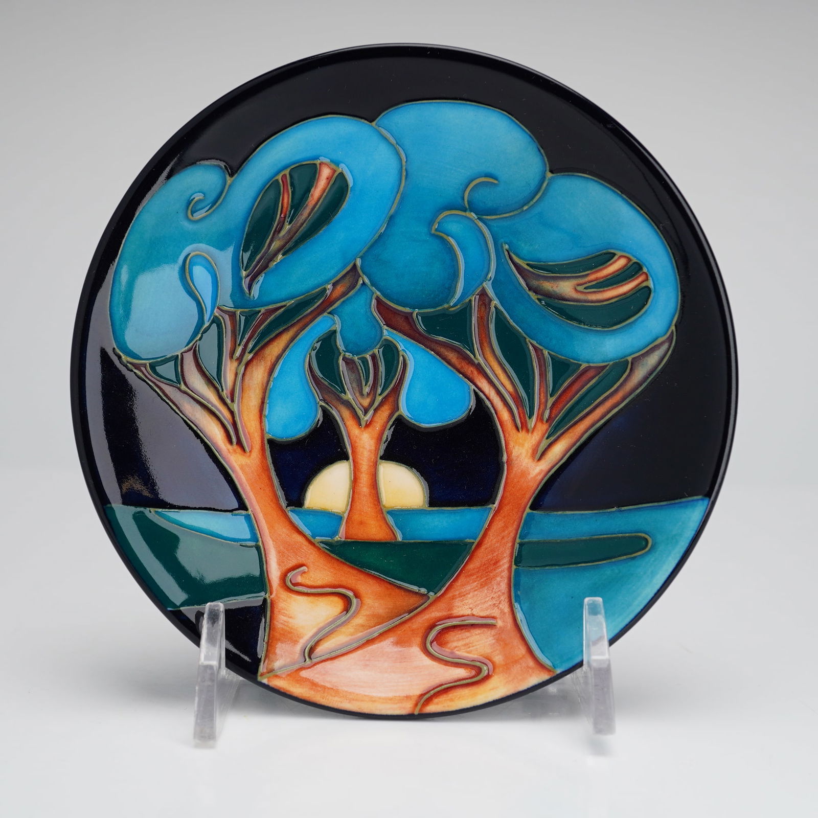 Moorcroft Night Forest Plate: A Moorcroft pottery plate in a night forest pattern. The circular plate features a landscape decoration with stylized trees in shades of blue and orange against a navy blue sky and a pale yellow moon.