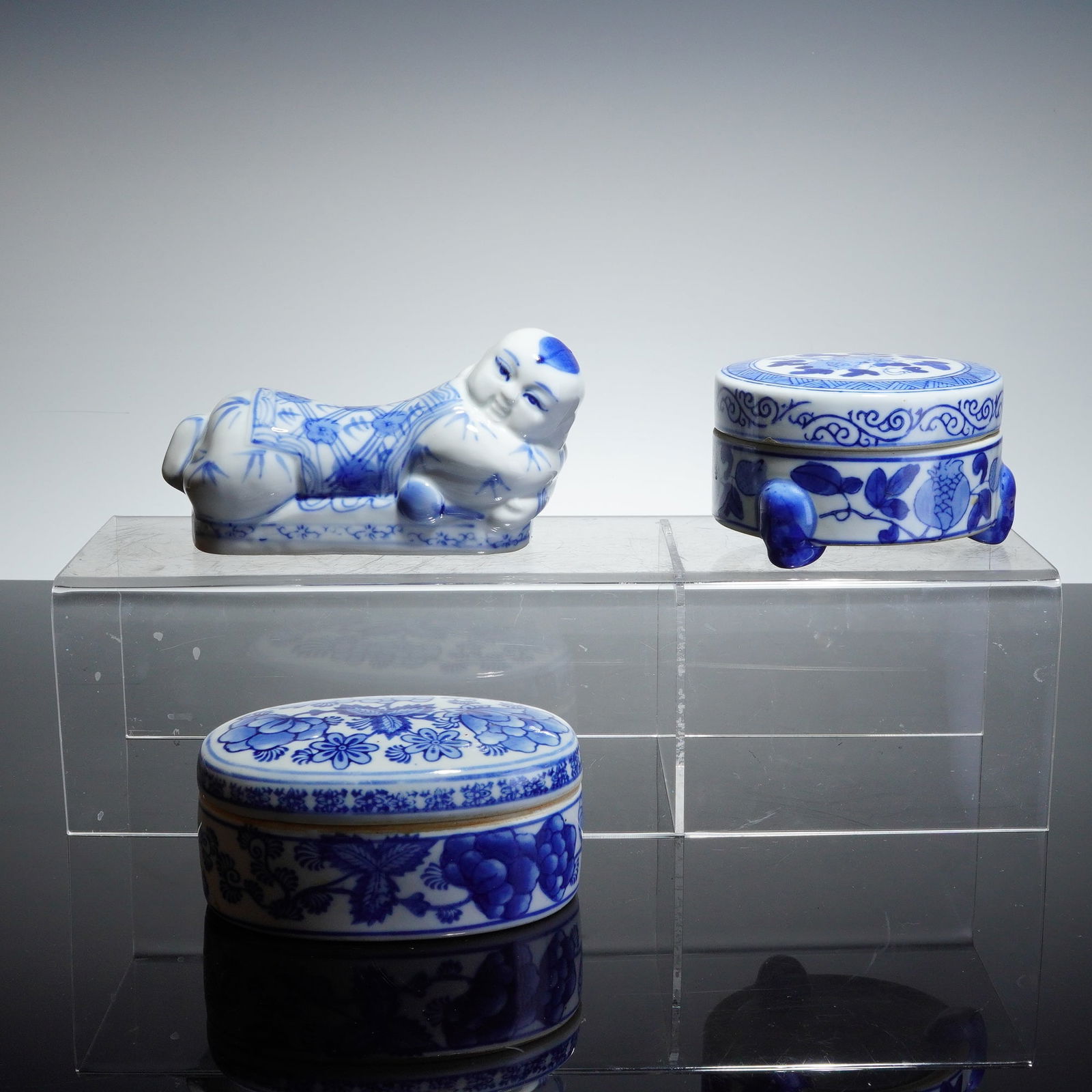 3pc Chinese Blue and White Porcelain Opium Pillow and Lidded Boxes: A trio of Chinese blue and white porcelain items executed in underglaze cobalt blue. The collection includes a reclining figure featuring a Chinese headrest in the shape of a child figure resting on a