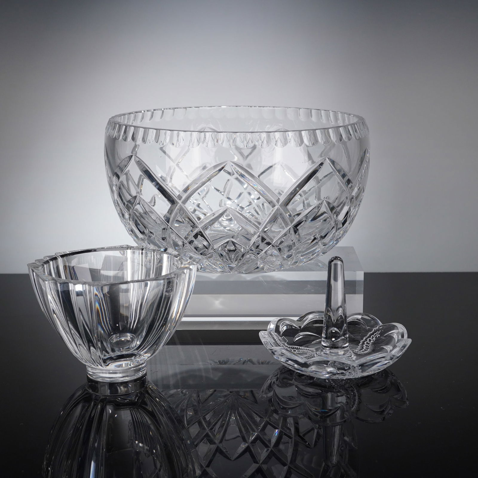 3pc Cut Crystal Bowls and Ring Dish, Waterford & Kosta Boda: A collection of three items of colorless cut glass and crystal that includes a large, deep serving bowl featuring extensive traditional diamond and cross-hatch cutting with a scalloped rim. This piece