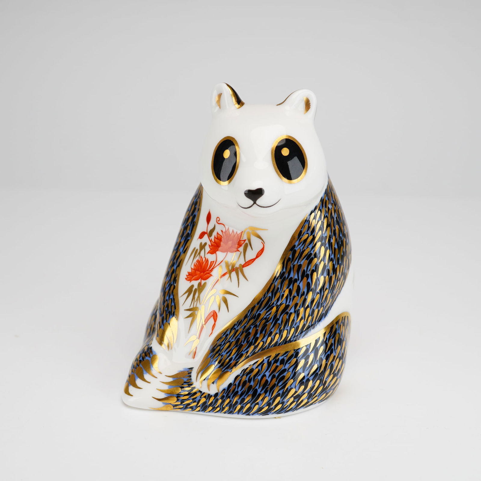 Royal Crown Derby Bone China Imari Paperweight, Panda: The figurine is decorated with an Imari-inspired pattern featuring cobalt blue and gold-tone ornamentation representing fur, accented with red and orange floral and bamboo motifs. The piece includes e