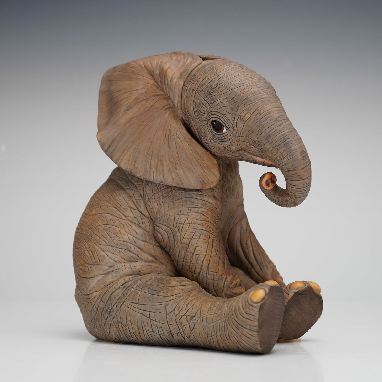 Lenox Porcelain Figurine, African Elephant Calf: Part of the Smithsonian Institution collection. This adorable elephant calf is seated with its head slightly tilted. Lenox backstamp. Issued: 1991 Dimensions: 5"L x 3.75"W x 6"H Country of Origin: Uni