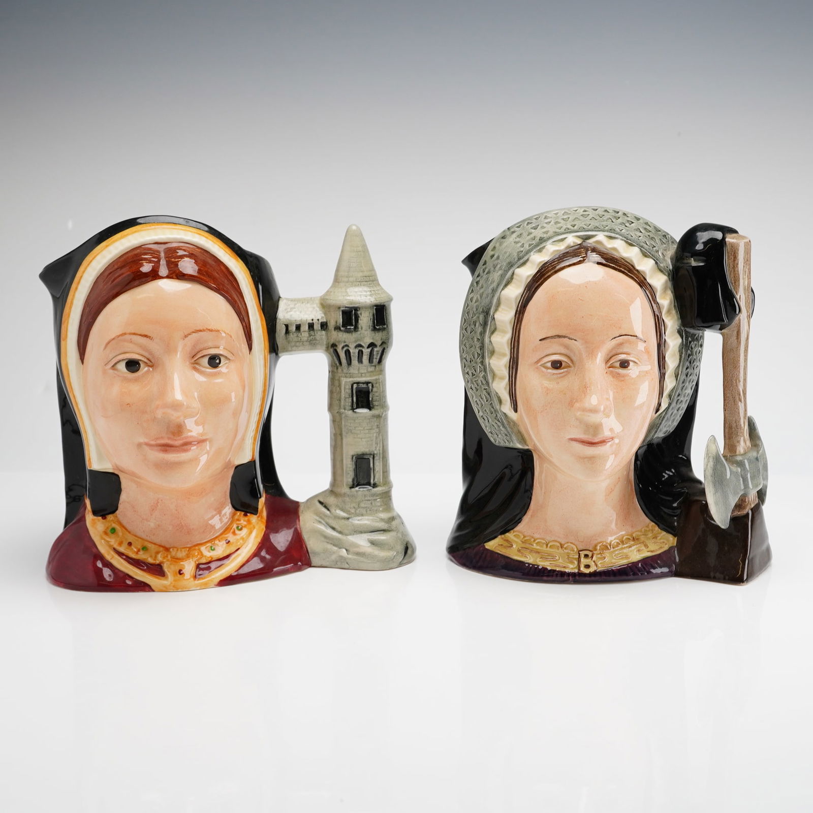 2pc Royal Doulton Character Jugs Catherine of Aragon and Anne Boleyn: This 2pc set of Royal Doulton ceramic character jugs includes Catherine of Aragon D6643 and Anne Boleyn D6644. Each item is modeled and finished with a high-gloss glaze. Catherine of Aragon is depicte