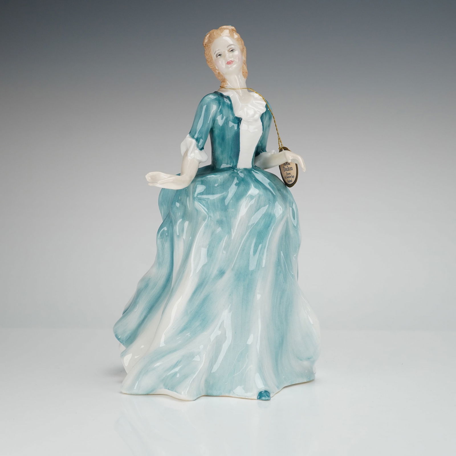 Royal Doulton Figurine Yvonne HN3038: The figure was designed by Adrian Hughes and copyrighted in 1988. The standing woman is depicted wearing a voluminous period gown featuring flowing teal blue and white coloration. The item retains its