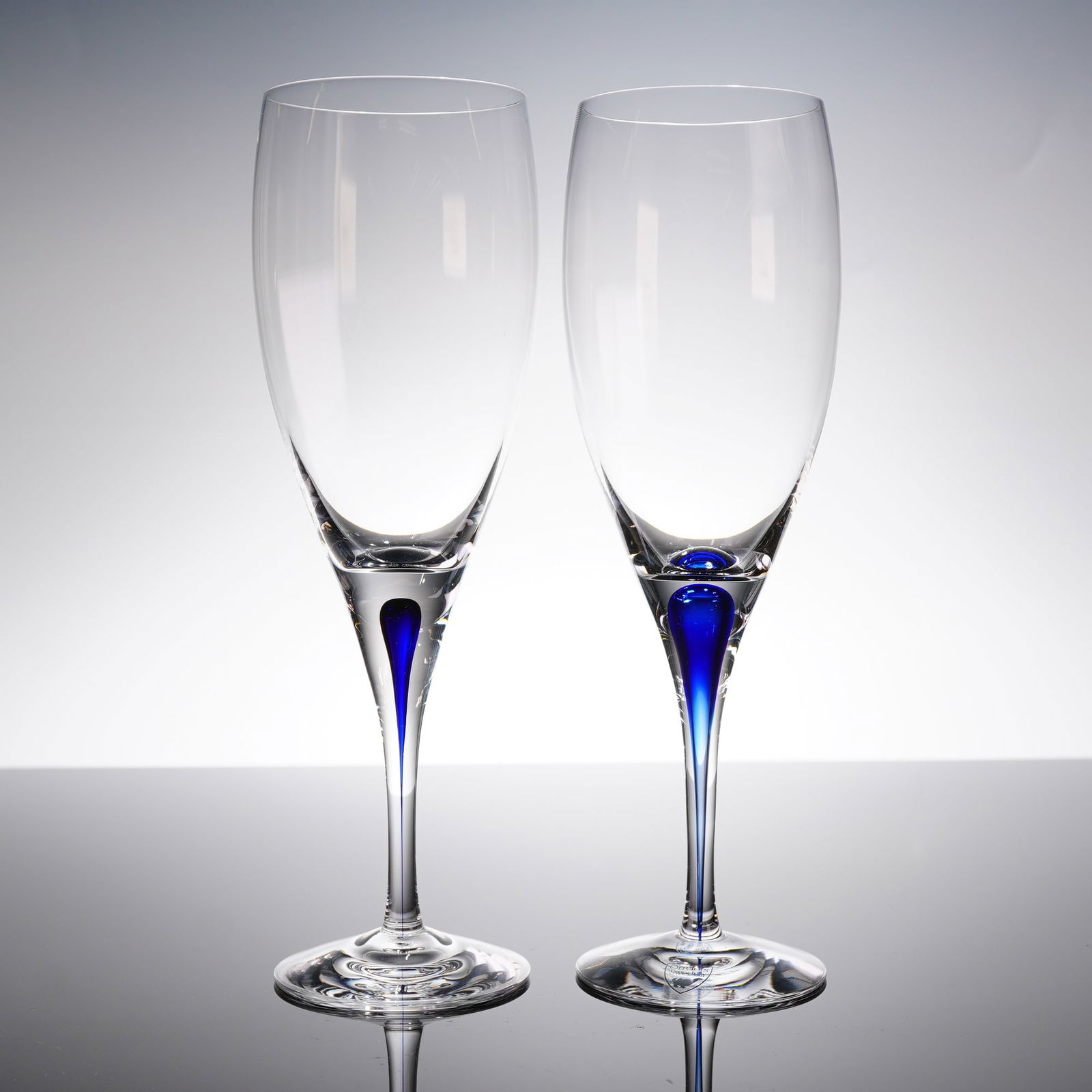 A Pair of Orrefors Intermezzo Blue Sparkling Wine Flutes: A pair of Orrefors Intermezzo Blue wine glasses, specifically designed as tall, slender champagne fi?utes. These 2pc glasses are crafted from clear crystal in a contemporary Scandinavian style. The de