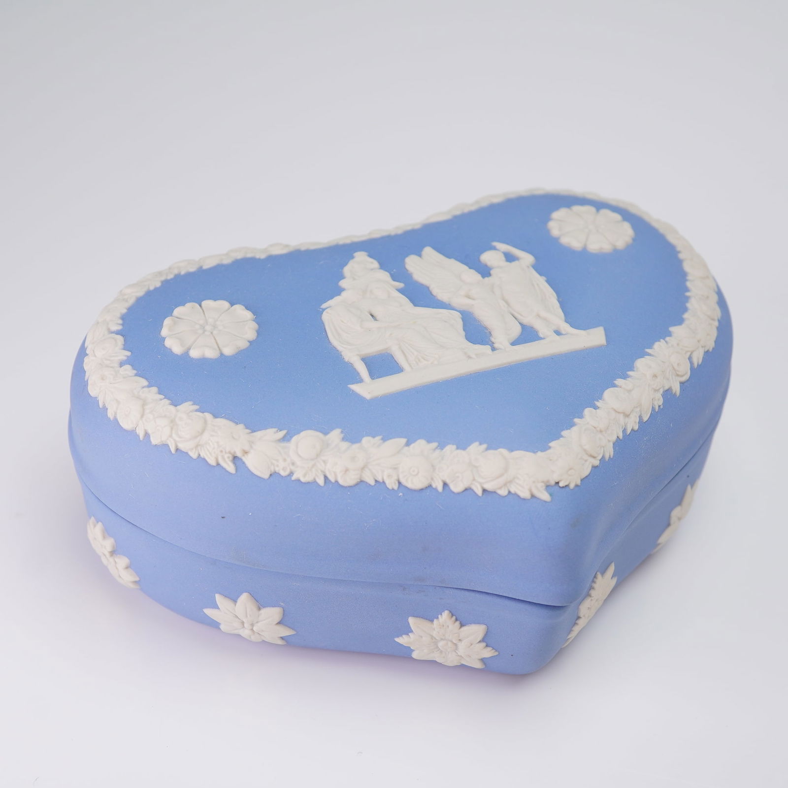Wedgwood Blue Jasperware Heart Shaped Lidded Box: This is a Wedgwood Jasperware lidded heart shaped box executed in the neoclassical style. The body and lid are crafted from matte pastel blue ceramic, featuring applied white bas-relief decoration.