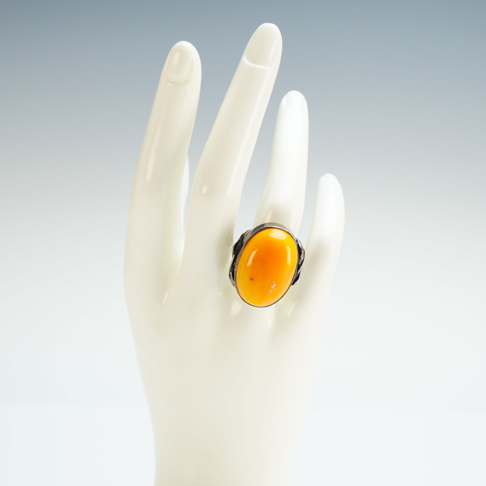 Sterling Silver Ring with Egg Yolk Amber: A sterling silver ring with a large butterscotch yellow oval stone. Each shoulder is decorated with small leaves. The band is marked 925 with a head facing right hallmark. Weight includes non-sterling