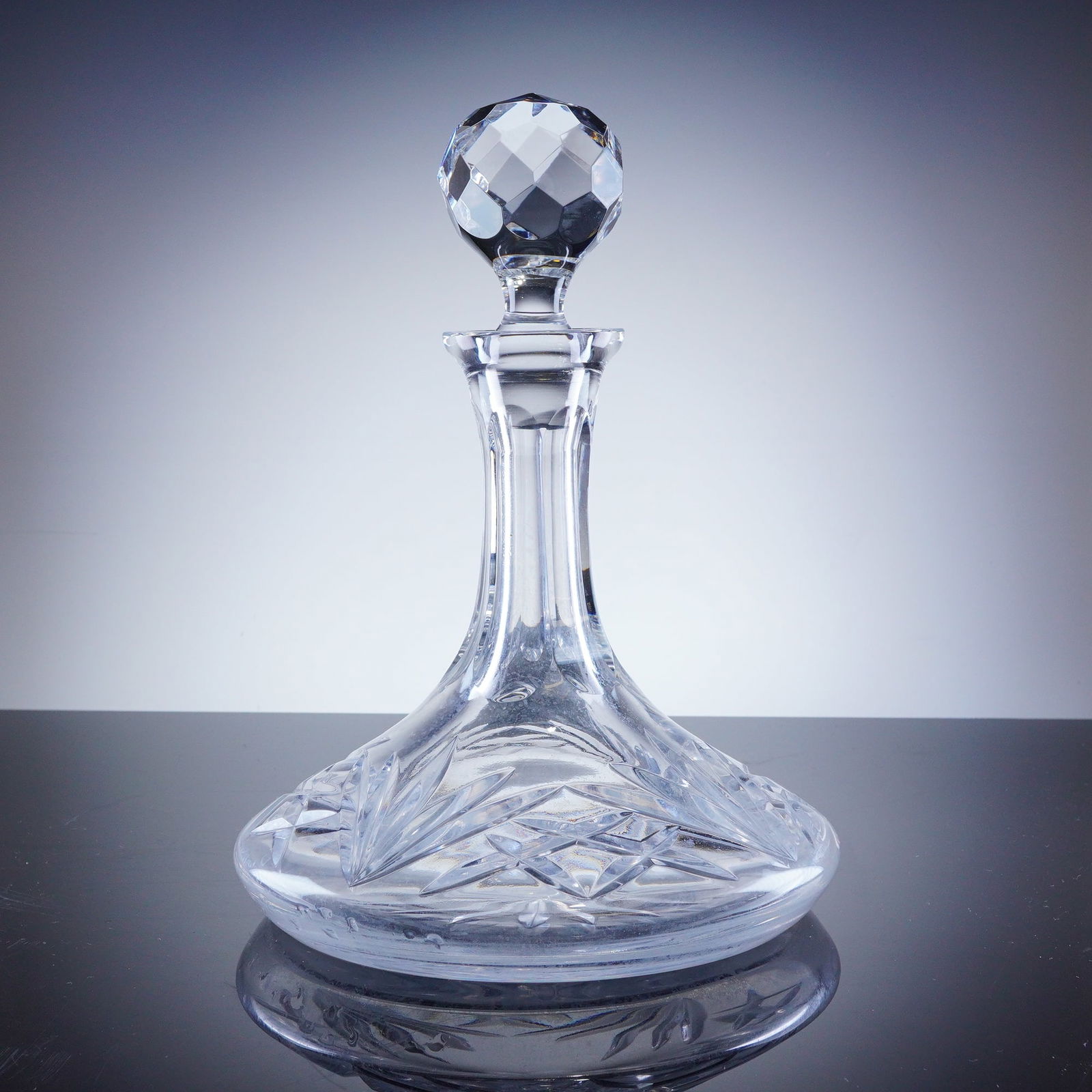 Crystal Ships Decanter with Stopper: The vessel is constructed in the traditional ships decanter form, featuring a broad, stable base tapering into a tall, slender neck. The body is extensively decorated with deep geometric cutting, incl