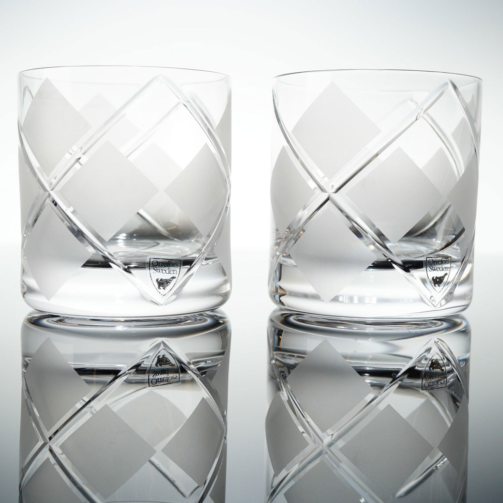 Pair of Orrefors Argyle Crystal Double Old Fashioned Glasses: A pair of Orrefors Argyle crystal double old fashioned glasses. These heavy, cylindrical rocks glasses feature a thick base and are decorated with a distinctive frosted checkered paterned design. The