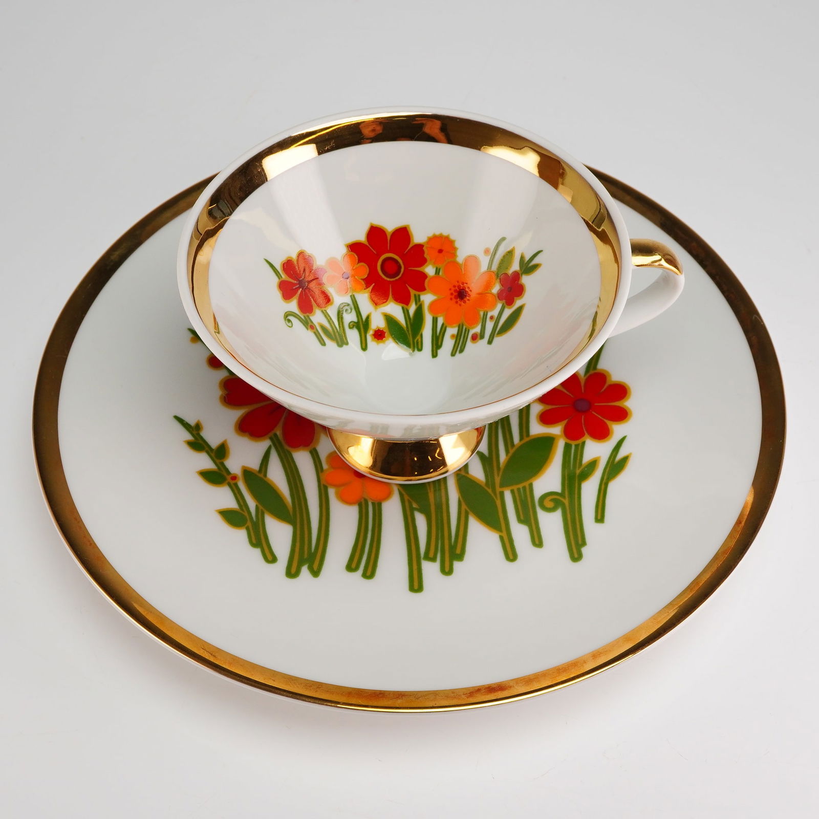 2pc Mitterteich Bavaria Porcelain Tea Set, Mid-Century Floral: The cup and saucer set is constructed of white glazed porcelain and features a distinctive Mid-Century style floral decoration. The stylized blossoms are rendered in flat applications of red, orange,