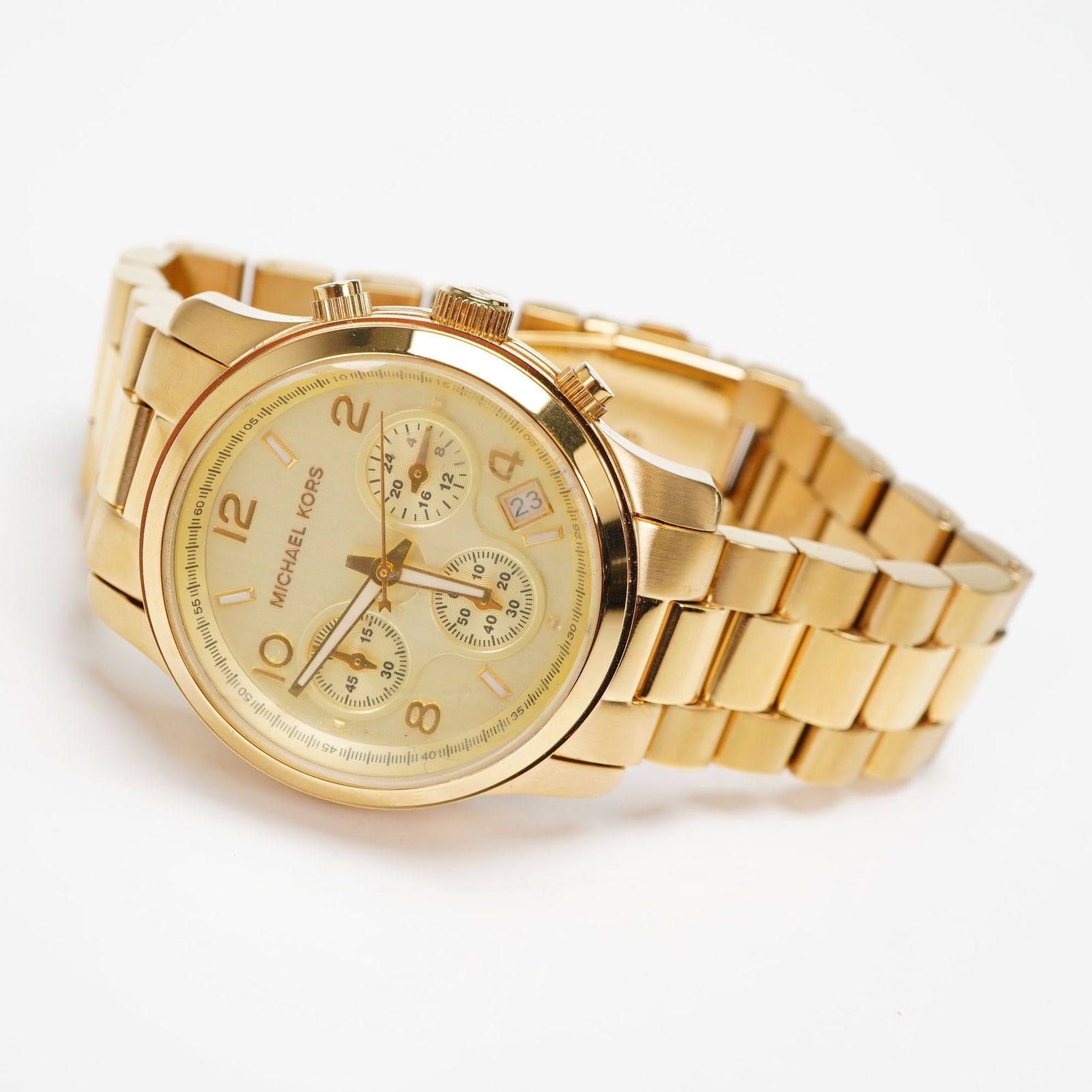 Michael Kors Runway Chronograph Gold Tone Watch MK5055: A Michael Kors Runway Chronograph wristwatch, model MK-5055, constructed of gold-toned stainless steel. The watch features a champagne dial with three chronograph sub-dials and a date aperture located