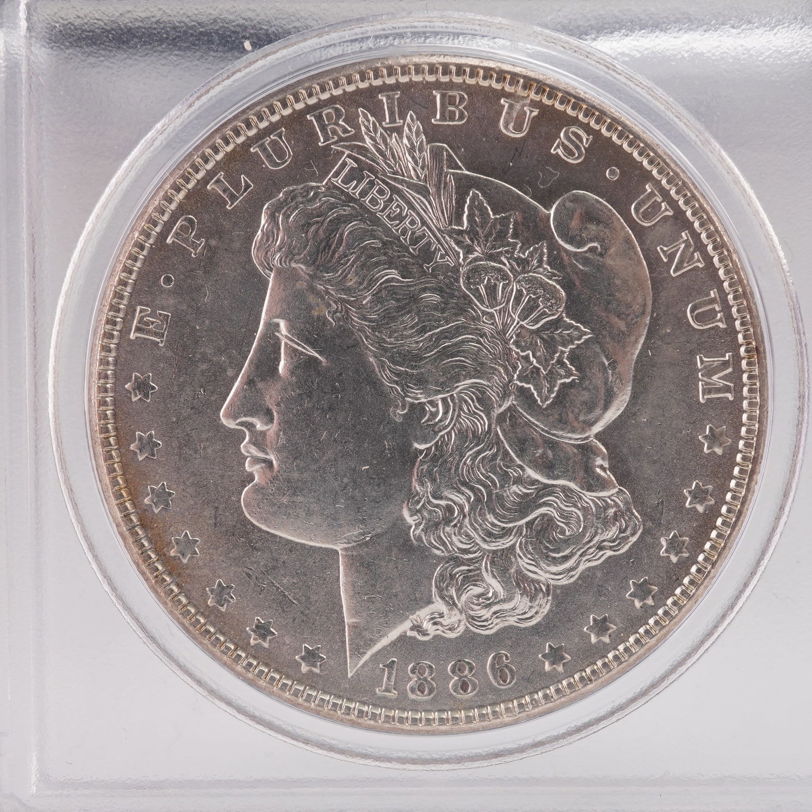 1886 Morgan Silver Dollar: This 1886 Morgan Silver Dollar showcases Liberty in profile wearing a Phrygian cap adorned with wheat and cotton, bordered by stars and the inscription E PLURIBUS UNUM along with the year 1886. The re