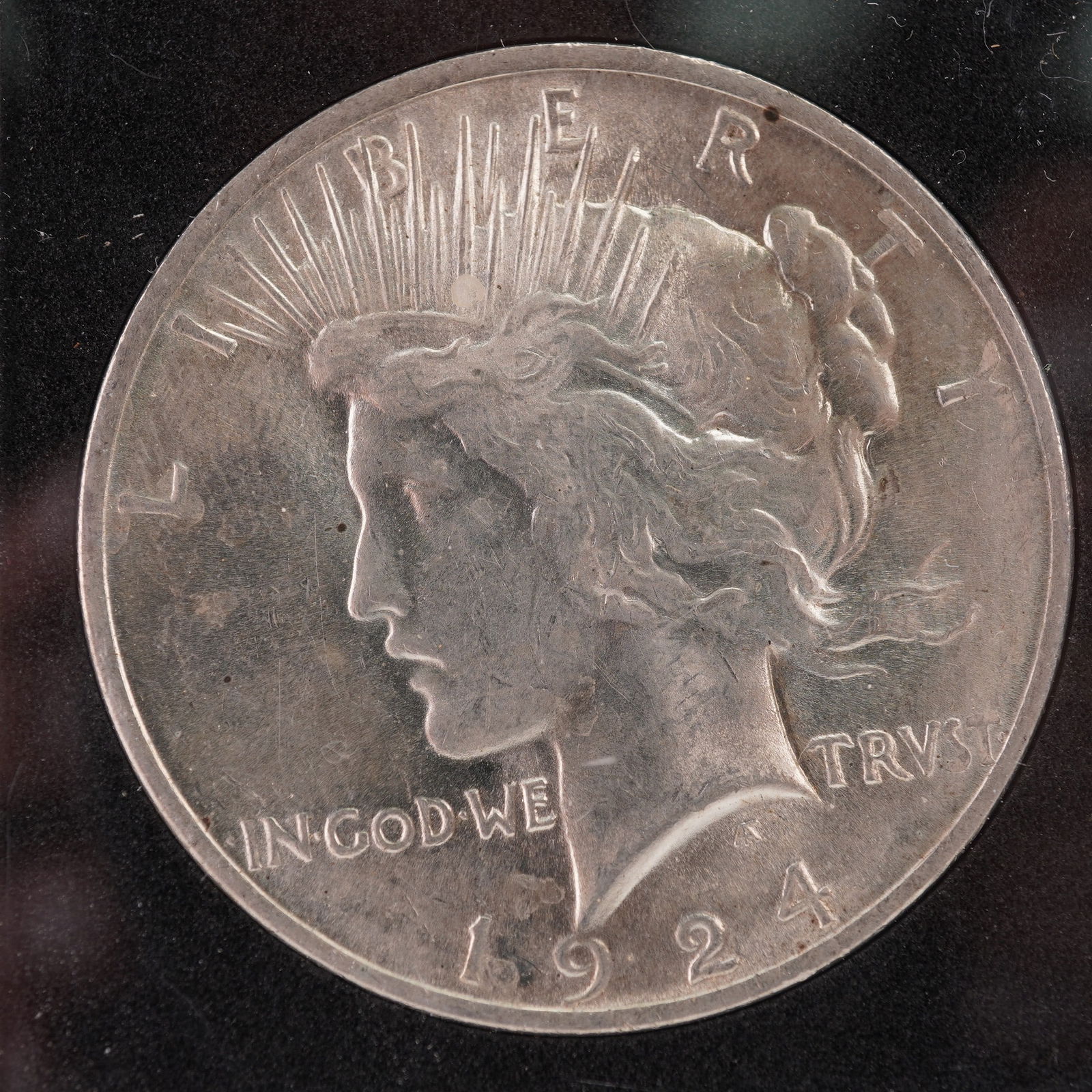 1924 Peace Silver Dollar: This 1924 Peace Silver Dollar is housed in a protective case. The obverse, designed by Anthony de Francisci, shows Liberty facing left wearing a radiate crown, with the inscriptions LIBERTY, IN GOD WE