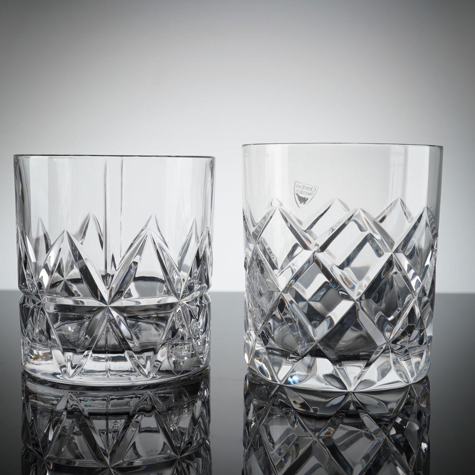 Pair of Orrefors Crystal Tumblers: A single piece of clear, colorless crystal atributed to the Swedish manufacturer Orrefors. The tumblers feature deep, angular, geometric faceting consistent with 20th-century Scandinavian design. The