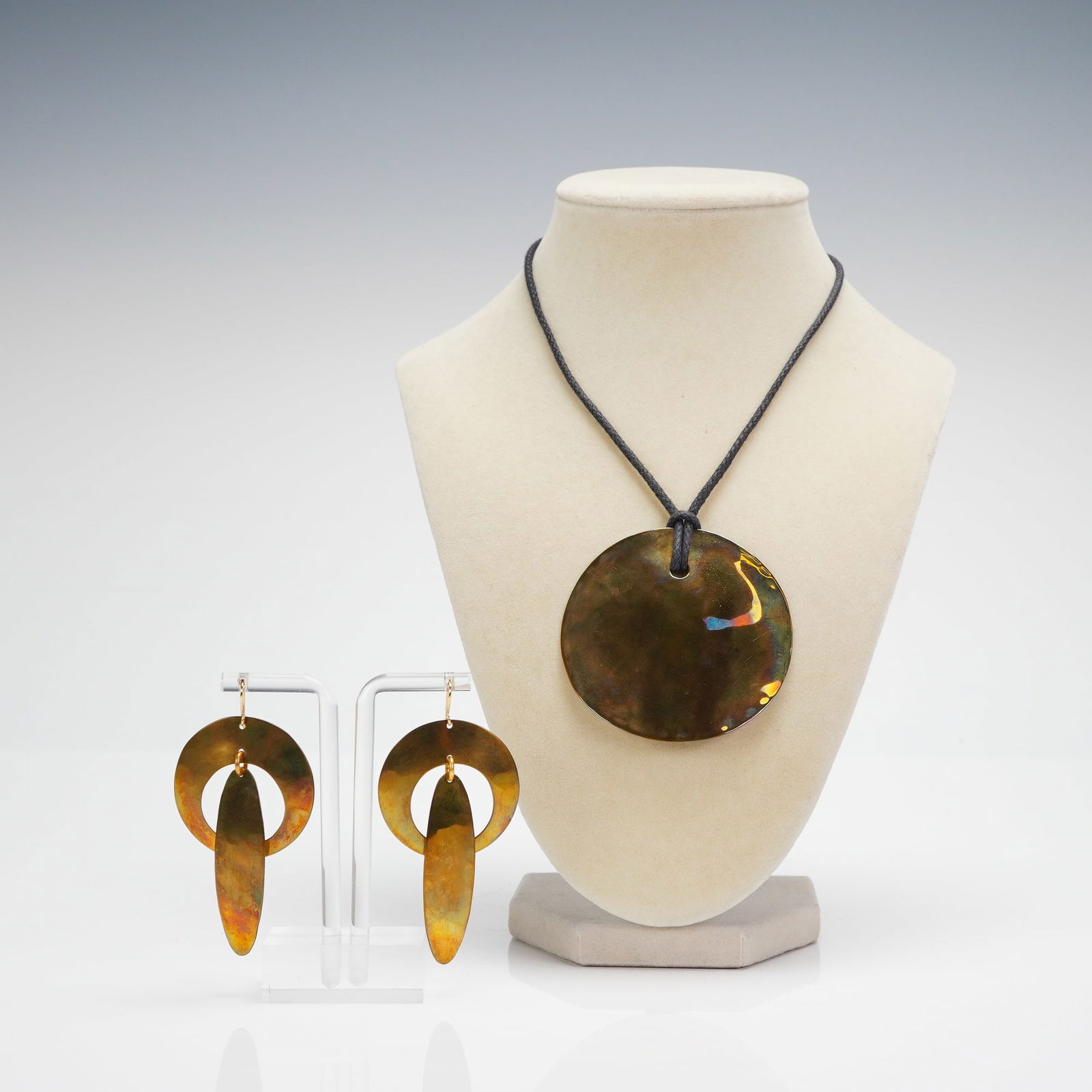 3pc RLM Studio Robert Lee Morris Modernist Pendant Necklace & Earrings: Consisting of a pendant necklace and a pair of dangle earrings constructed from brass. The necklace features a large, circular disc pendant suspended by a knot on a black braided cord and is stamped R