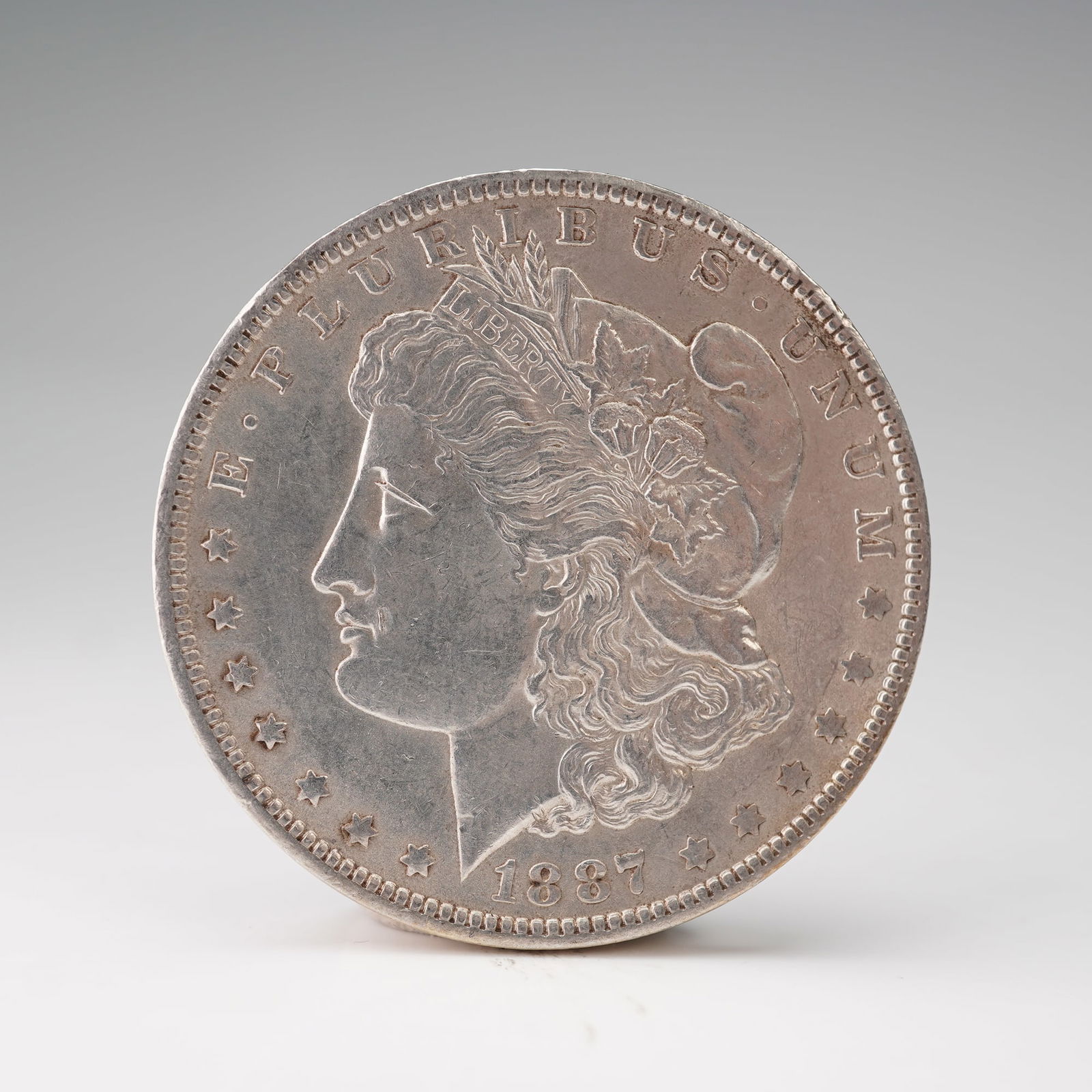 1887-O Morgan Silver Dollar: A piece of history with the obverse featuring a left-facing portrait of Liberty wearing a Phrygian cap adorned with wheat and cotton, symbolizing agricultural prosperity, surrounded by the inscription