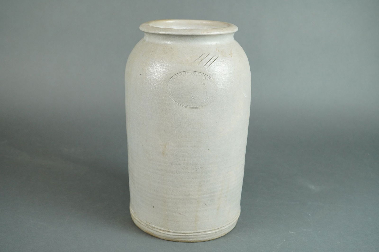 A Salt-Glazed Stoneware Storage Jar by W. Soper & Son, Wellington: A single, tall, cylindrical utilitarian storage jar, often referred to as a crock or pot, composed of salt-glazed stoneware. The vessel features a light gray-white finish consistent with the salt-glaz
