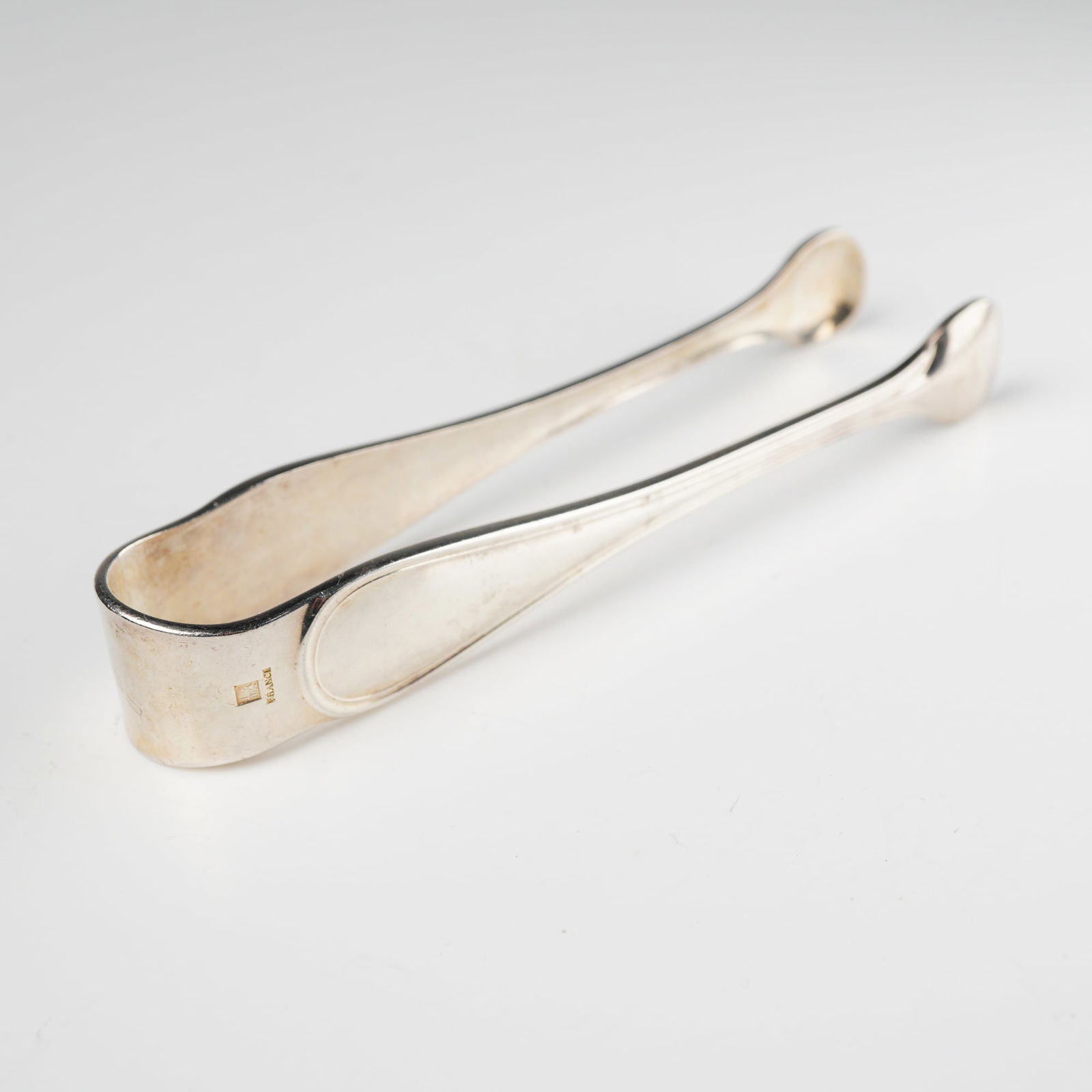 A Pair of Christofle Silver-Plated Sugar Tongs: A pair of Christofle silver-plated sugar tongs, featuring a classic, undecorated design with smoothly rounded ends. The interior of one arm is impressed with the brand name 'CHRISTOFLE', a square hall