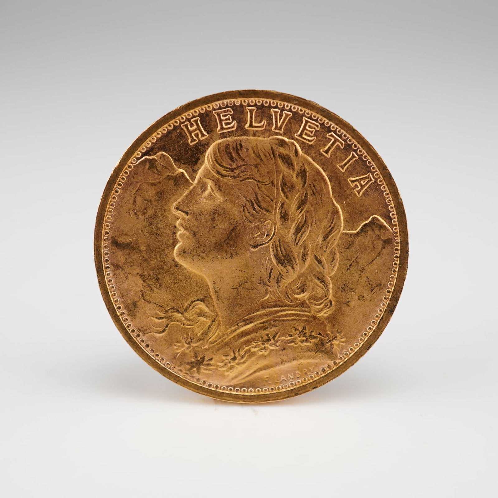 1947-B Swiss Vreneli Helvetia 20 Francs Gold Coin: Struck at the Bern Mint in Switzerland, featuring on the obverse the bust of a young woman from Oberhasli facing left with flowing tresses and a garland of edelweiss against a mountainous background,