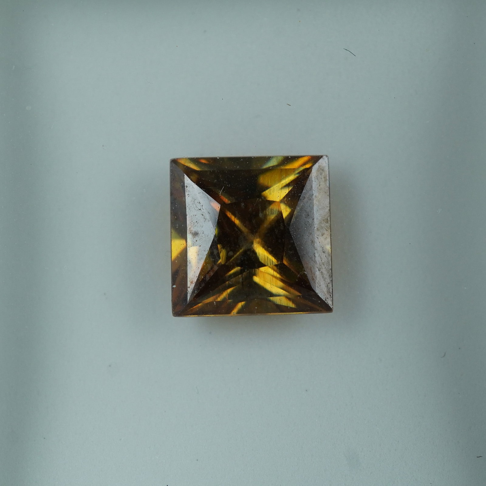 5.49 CT Russian Strontium Princess Cut Gemstone: Strontium gemstone weighing approximately 5.49 carats, cut in a princess shape with sharp facets and fiery brilliance. Exhibiting warm golden-brown tones, this stone is noted for its exceptional dispe