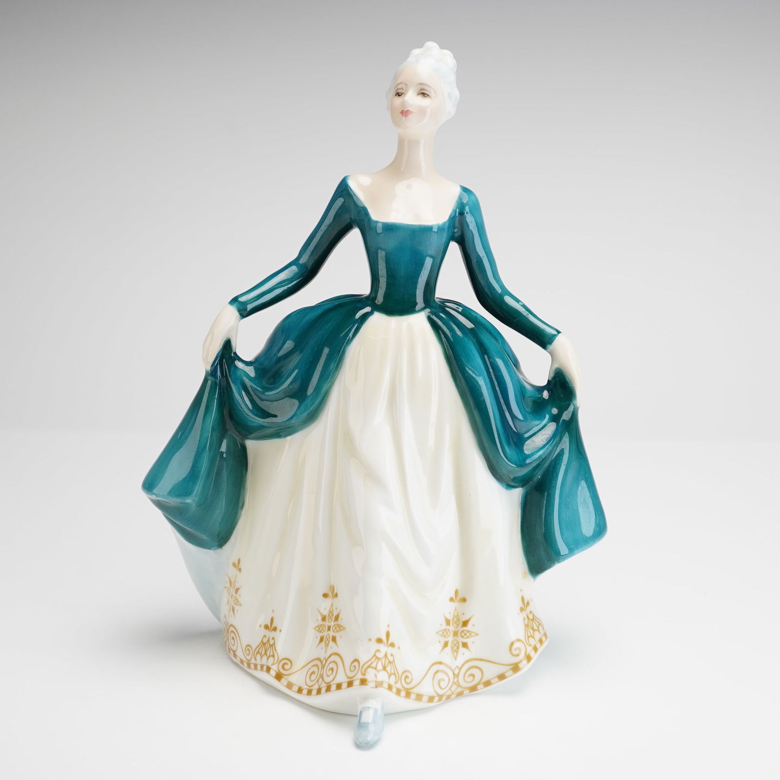 Royal Doulton Figurine Regal Lady HN 2709: The figurine depicts a woman in a period-style ballgown, designed and copyrighted in 1974. The gown features a glossy teal-green glaze on the bodice and overskirt, contrasting with a creamy white unde