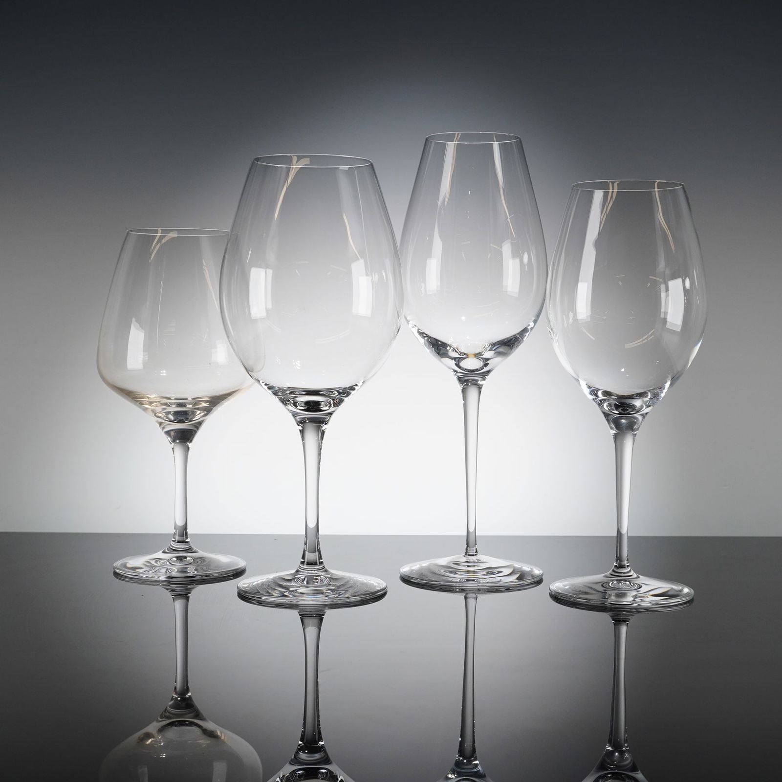 A Collection of Four Orrefors More Crystal Wine Glasses: A collection of four contemporary stemmed drinking glasses identified as the Orrefors More Wine patern. The glasses are crafted from clear crystal, featuring finely blown bowls of varying shapes and